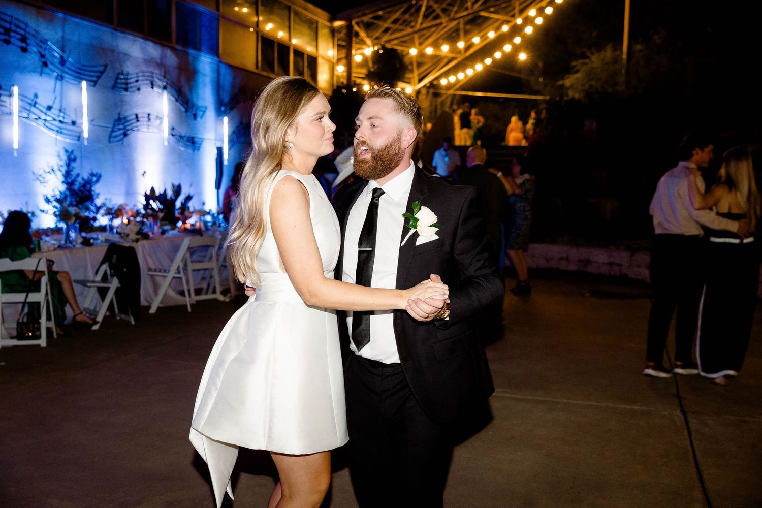 People dancing at a nighttime wedding reception under string lights and a tent.