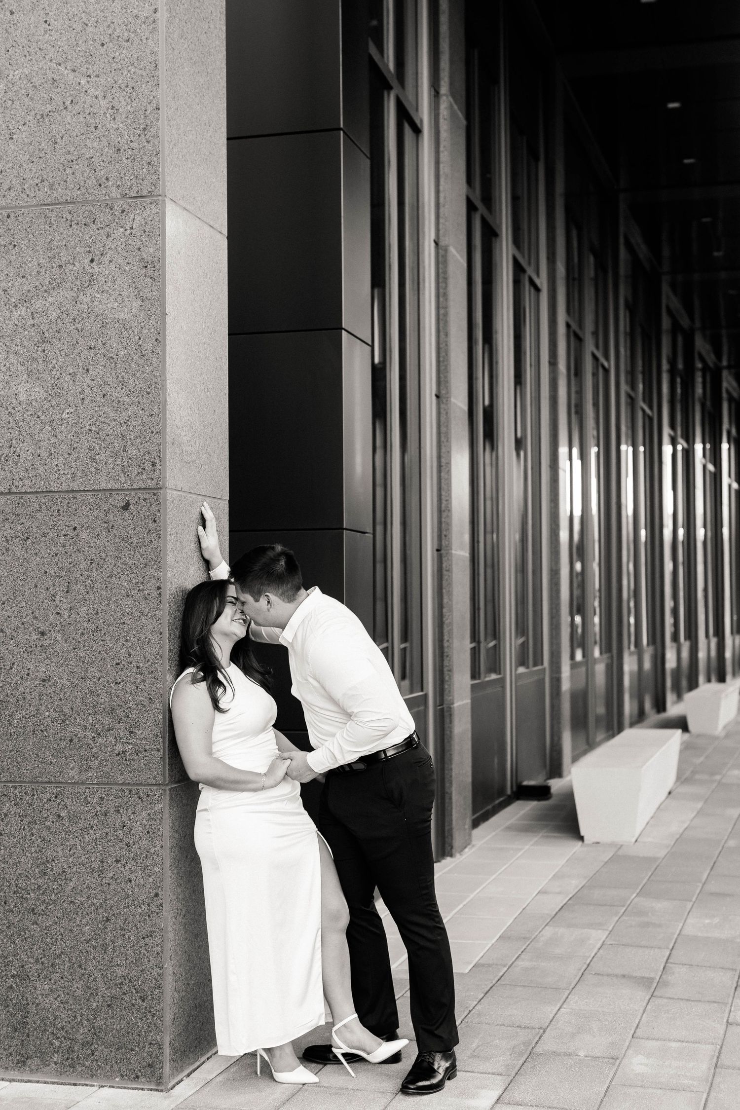 Black and white photo of romantic moment against modern building columns.