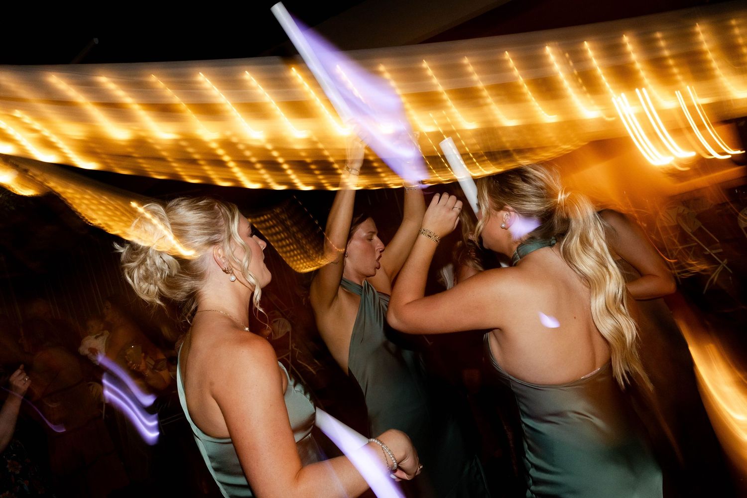 Wedding reception dance floor filled with guests dancing under warm lighting.