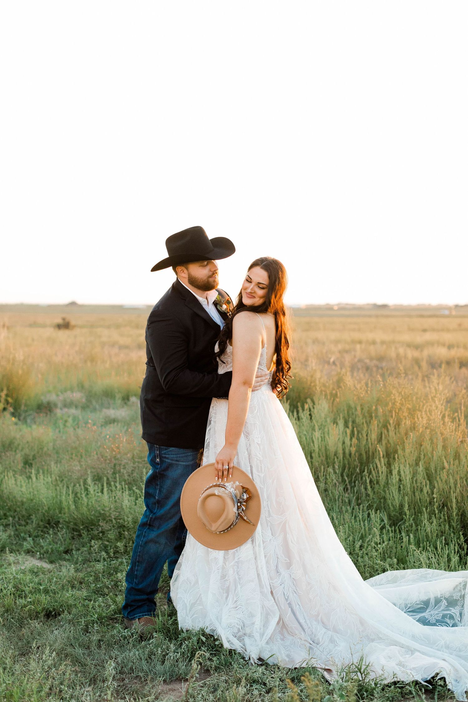 Newlywed couple in cowboy attire sharing intimate moment in prairie field.