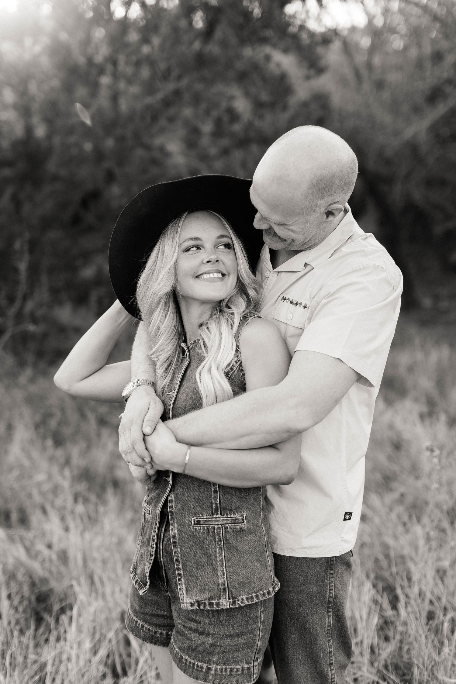 Romantic couple in western attire posing in a rustic field setting.