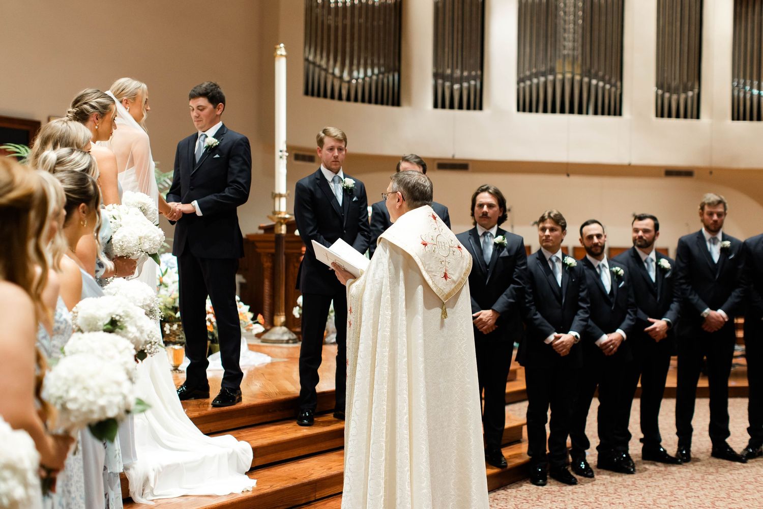 Wedding ceremony participants lined up in church sanctuary with organ pipes visible.
