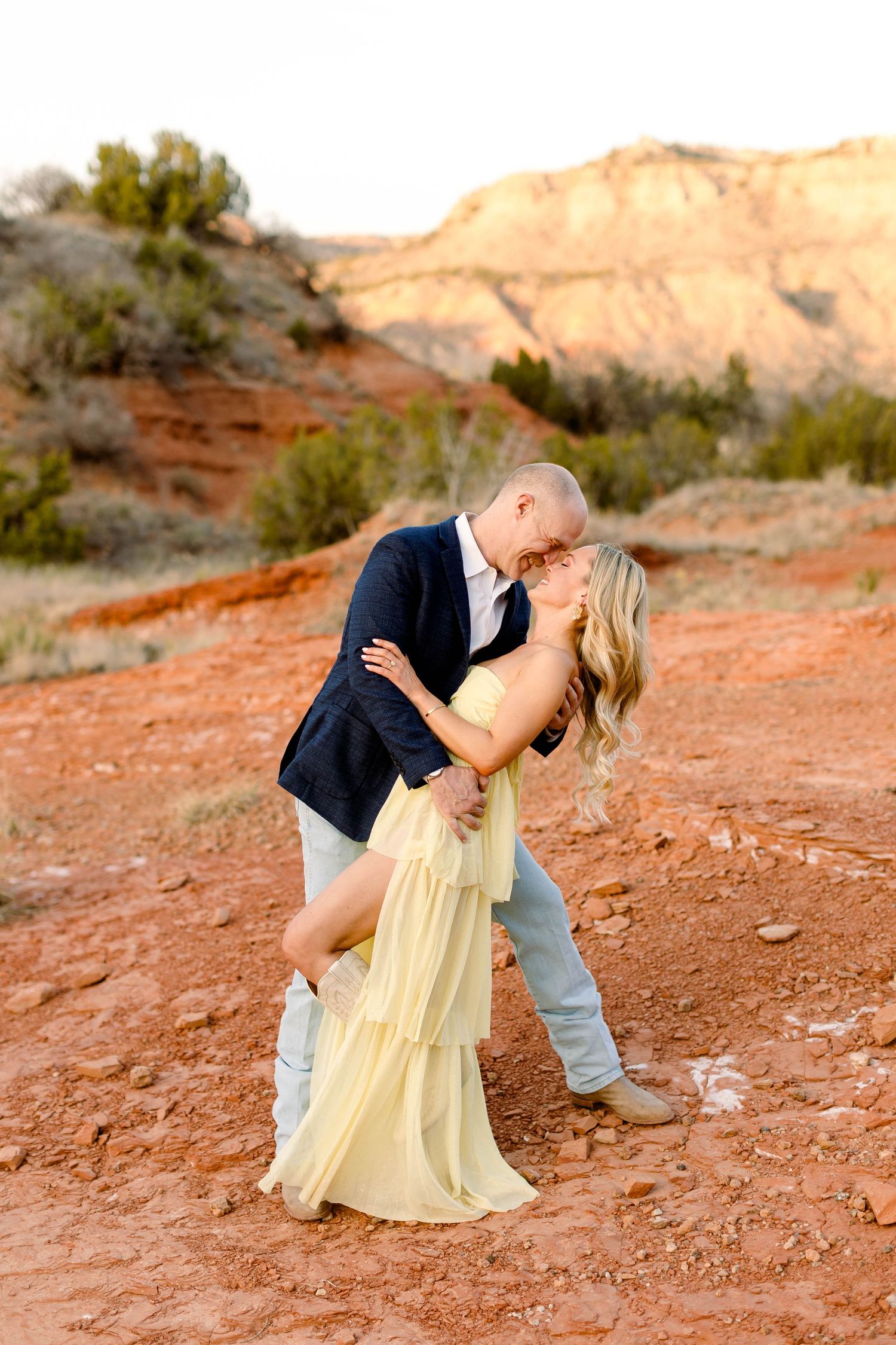 A romantic dip pose between a couple on red desert terrain at sunset.