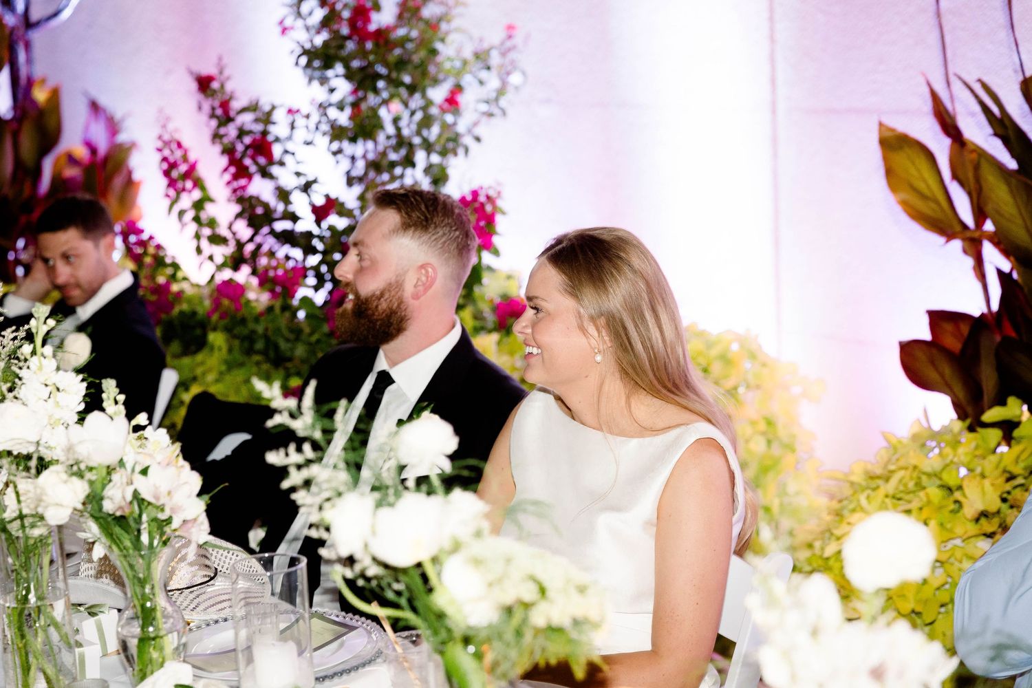 Wedding reception table decorated with elegant floral arrangements and white linens at an indoor venue.