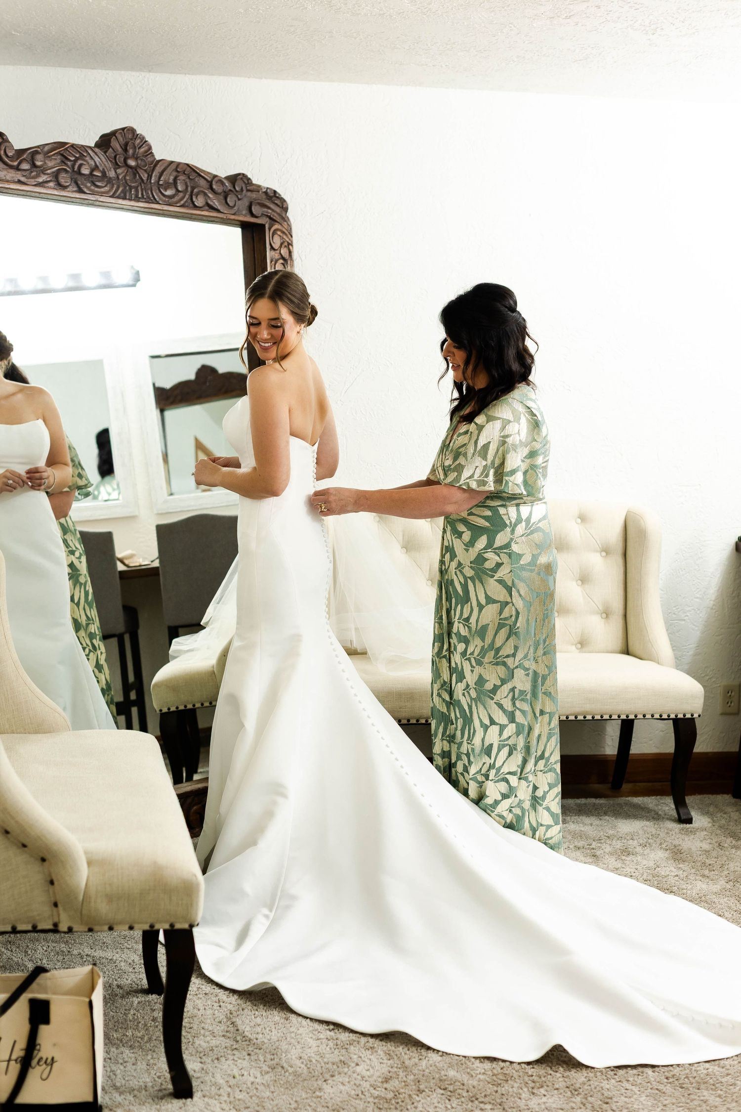 A wedding dress being fitted in an elegant dressing room with an ornate mirror.