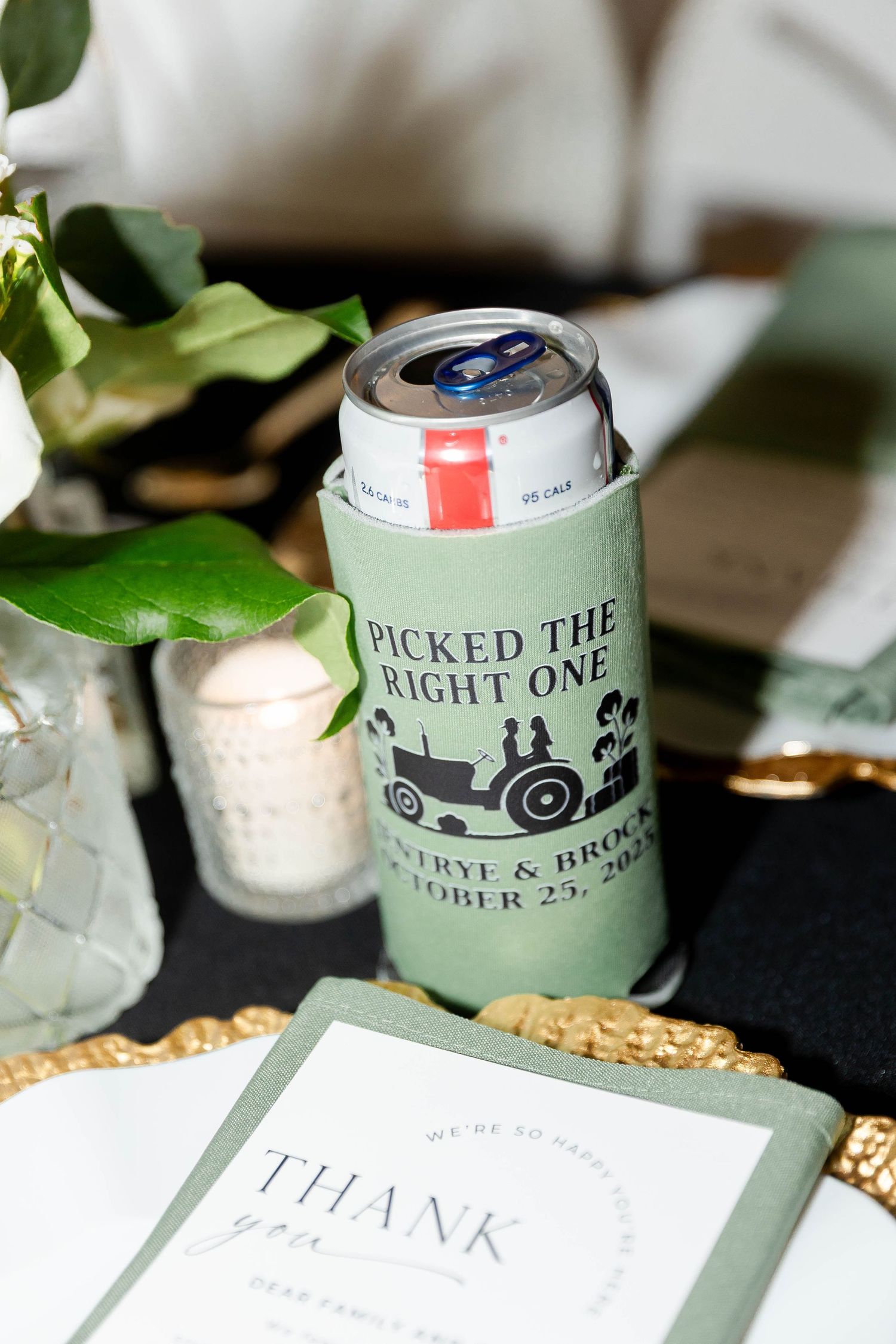 Wedding favor koozies and thank you cards displayed with greenery and rustic decor.