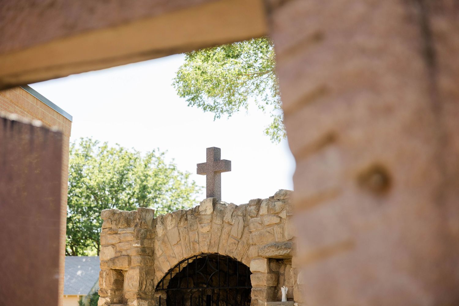 A stone archway with a cross on top is framed against a bright sky.