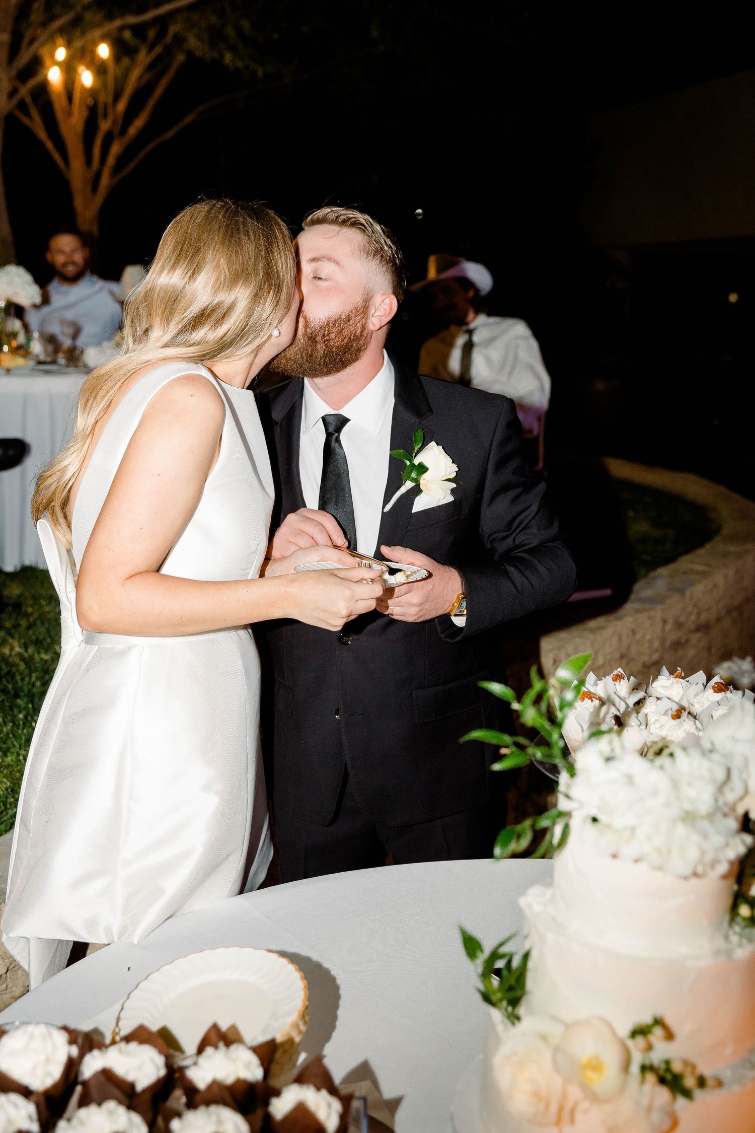 Newlyweds cutting their white tiered wedding cake decorated with fresh flowers.