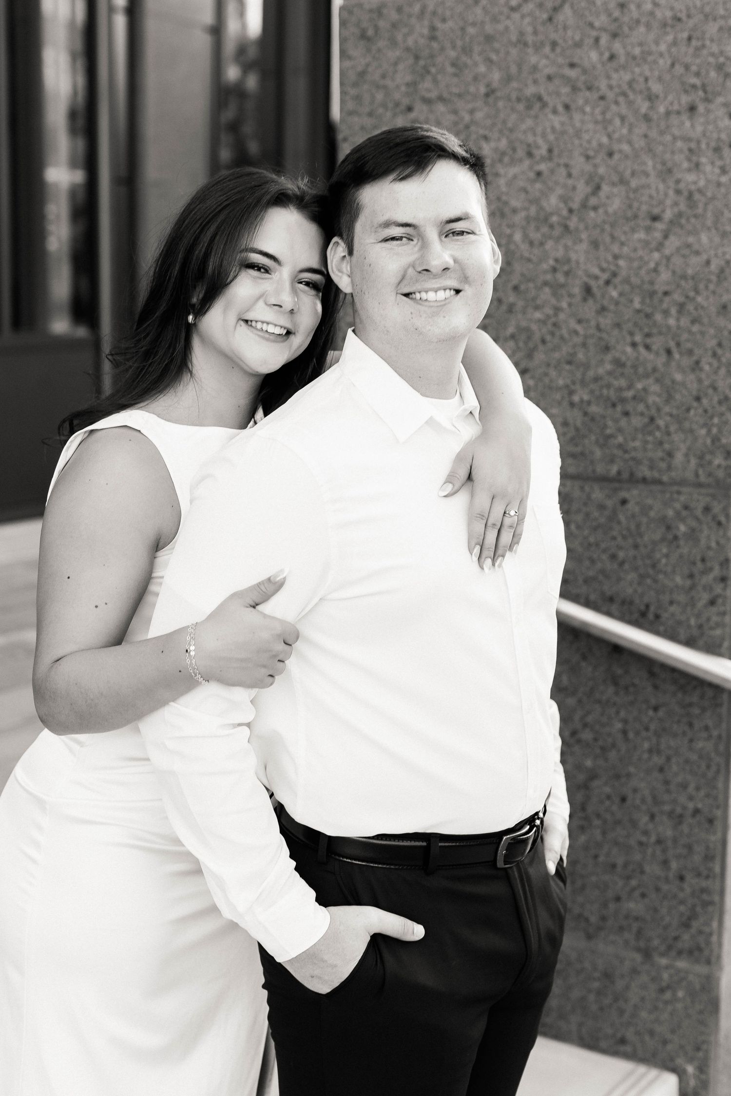 A playful engagement photo session showing a couple in white and black outfits against a gray wall.