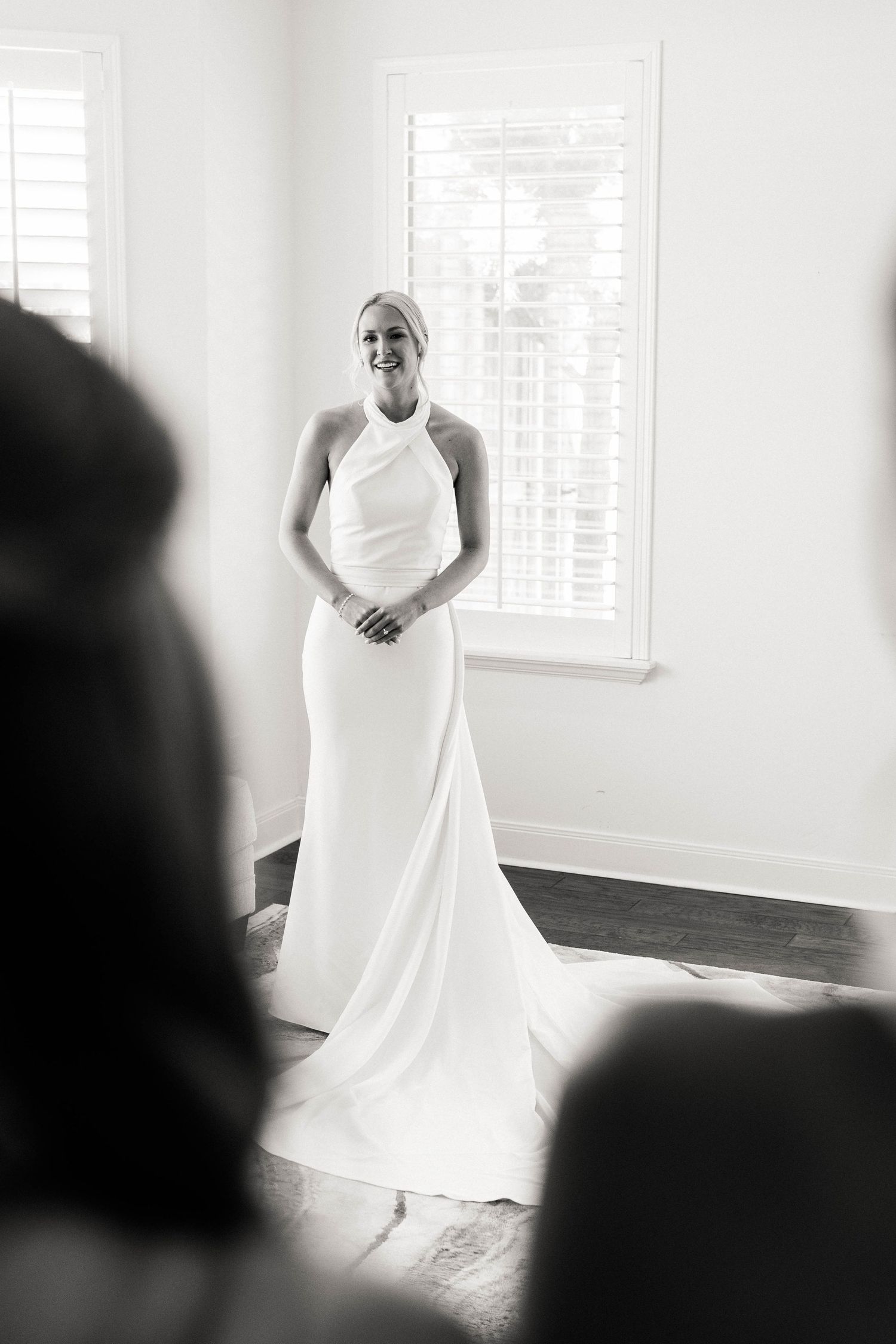 A flowing white wedding dress is captured in a bright, minimalist setting with window light.