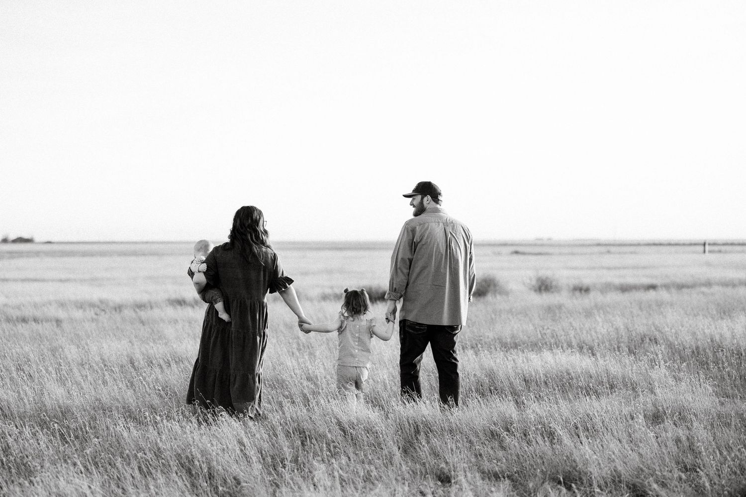 A family stands together in a vast prairie field with tall grass swaying in black and white photography.