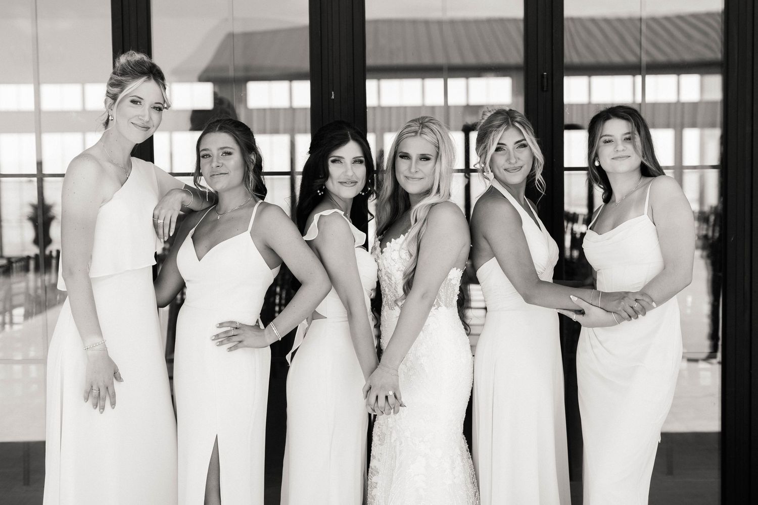 Bridesmaids in elegant white dresses pose together in a modern venue.
