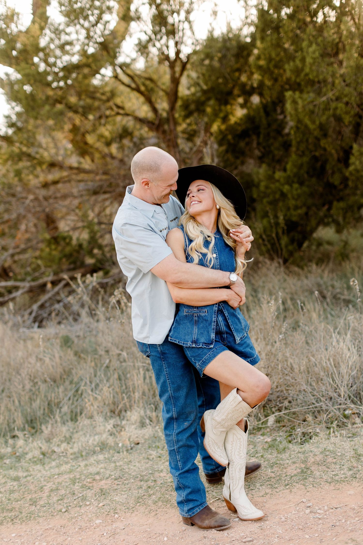 Romantic couple in matching denim outfits embrace on a dirt path during golden hour photoshoot.