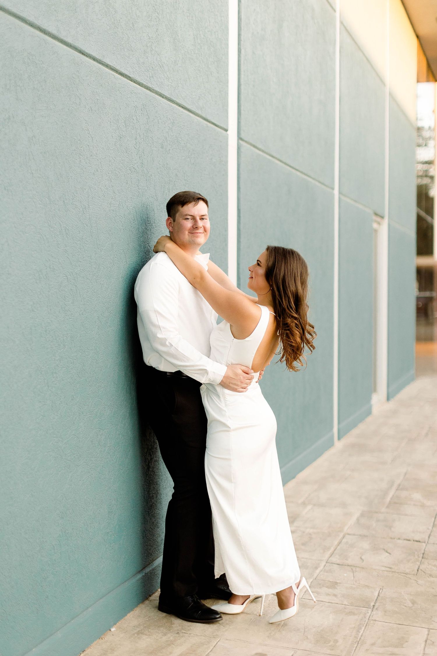 A couple in formal attire poses elegantly against a modern architectural backdrop.