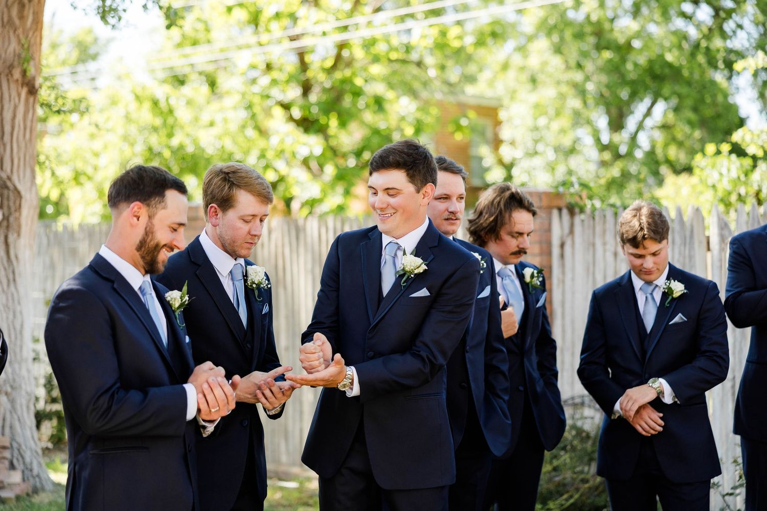 Wedding party groomsmen in navy suits laughing together outside.
