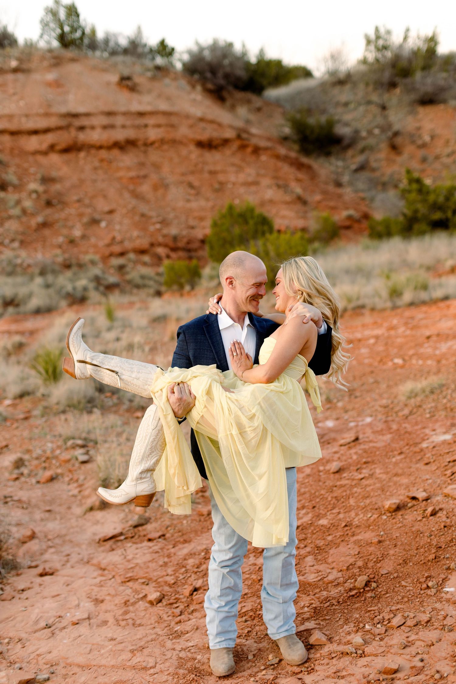 A couple shares a romantic lift pose against dramatic red rock formations.