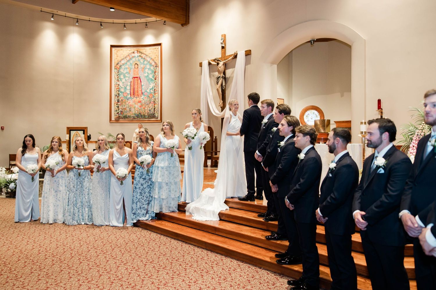 Wide view of wedding ceremony in church sanctuary with wedding party and guests.