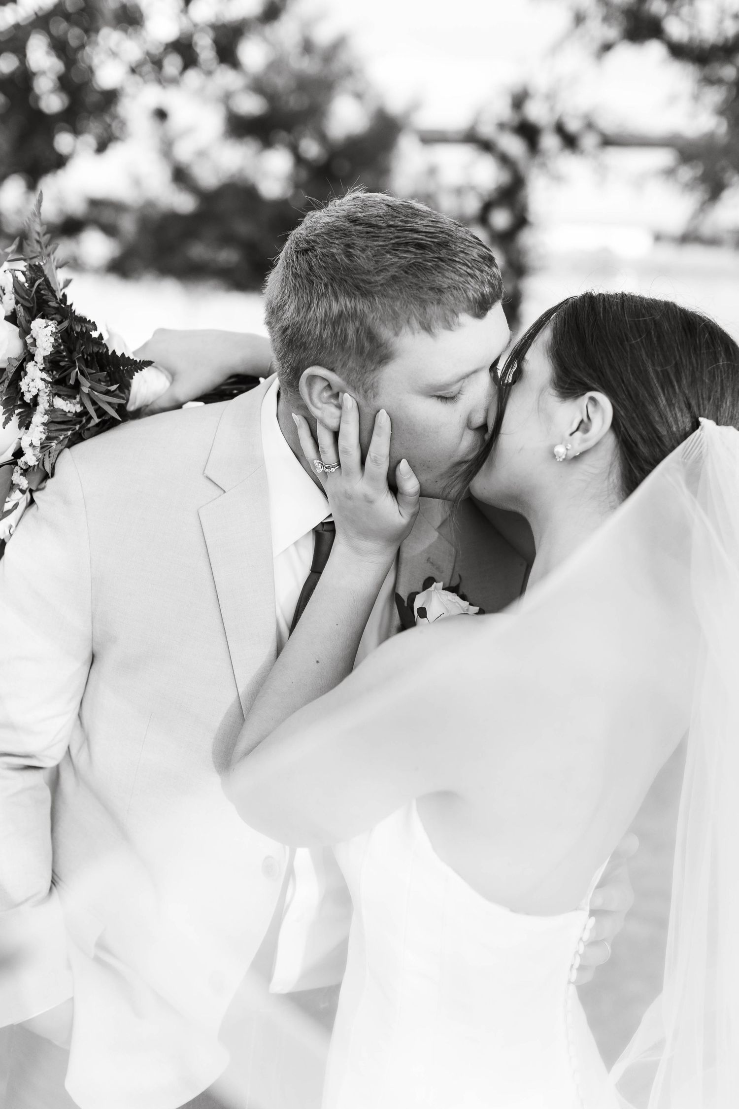 A romantic black and white wedding photo showing a tender kiss between newlyweds in traditional wedding attire.