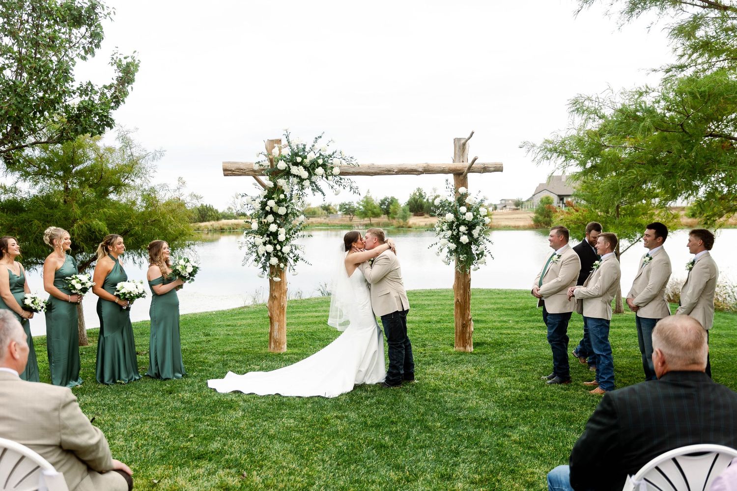A wedding ceremony and celebration takes place outdoors with bridesmaids in blue dresses and groomsmen in tan suits.