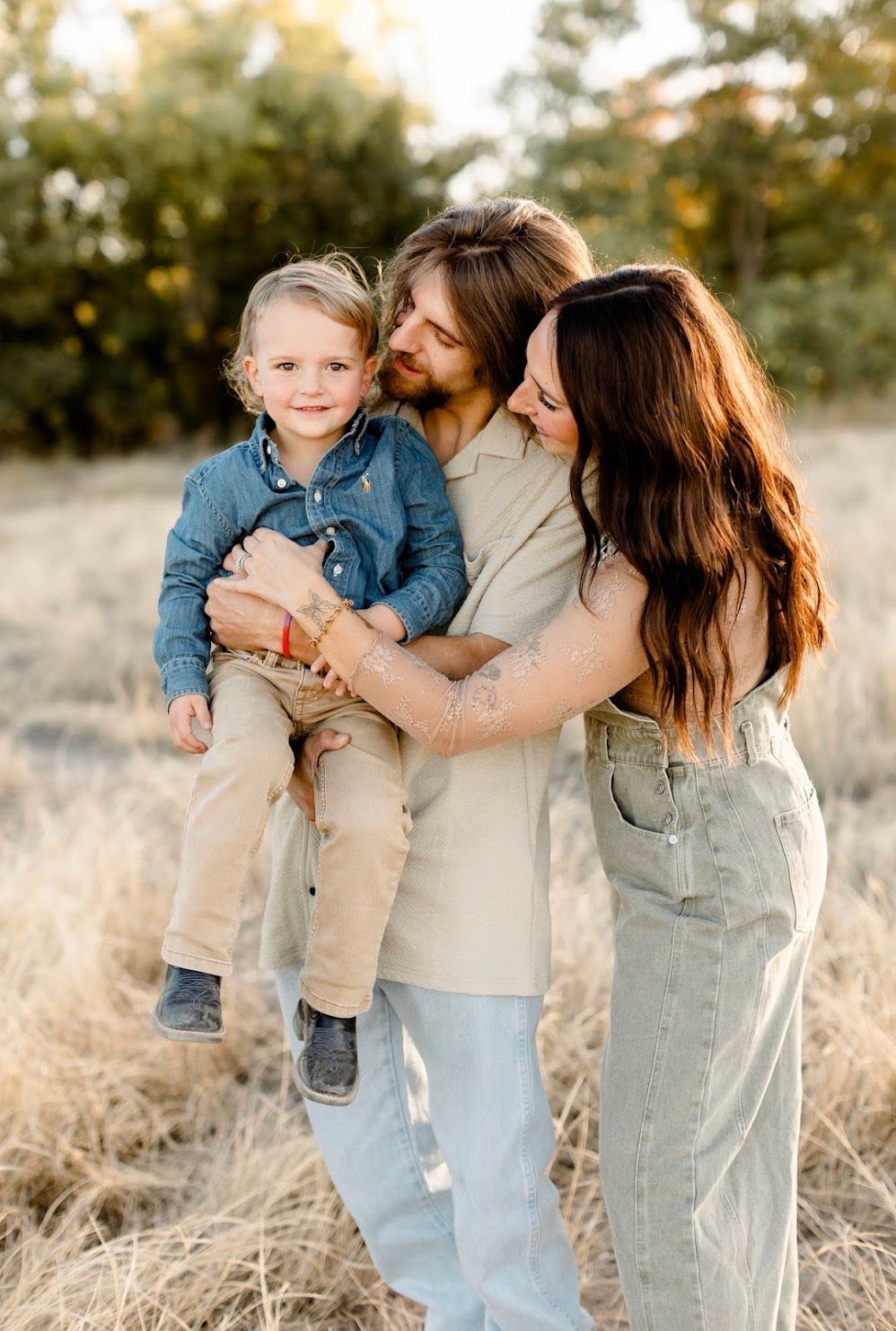 A family shares tender moments together in a sun-lit field wearing coordinated denim and neutral tones.
