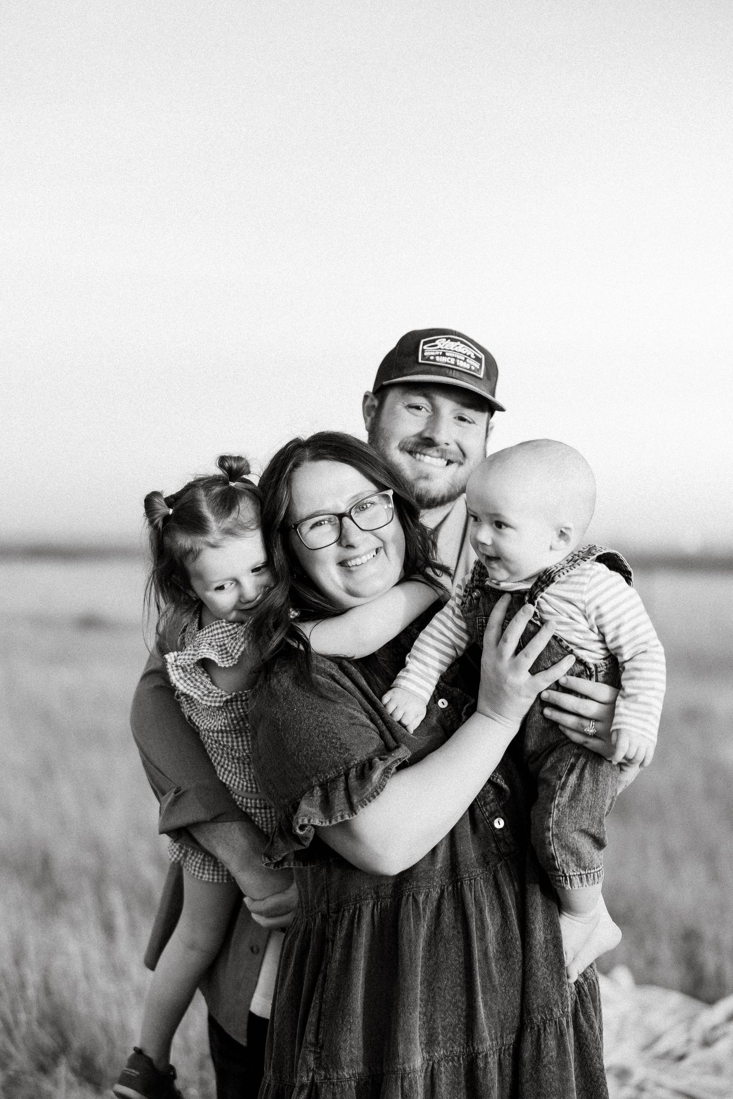 Black and white photo series showing joyful family moments in a field with matching striped outfits.