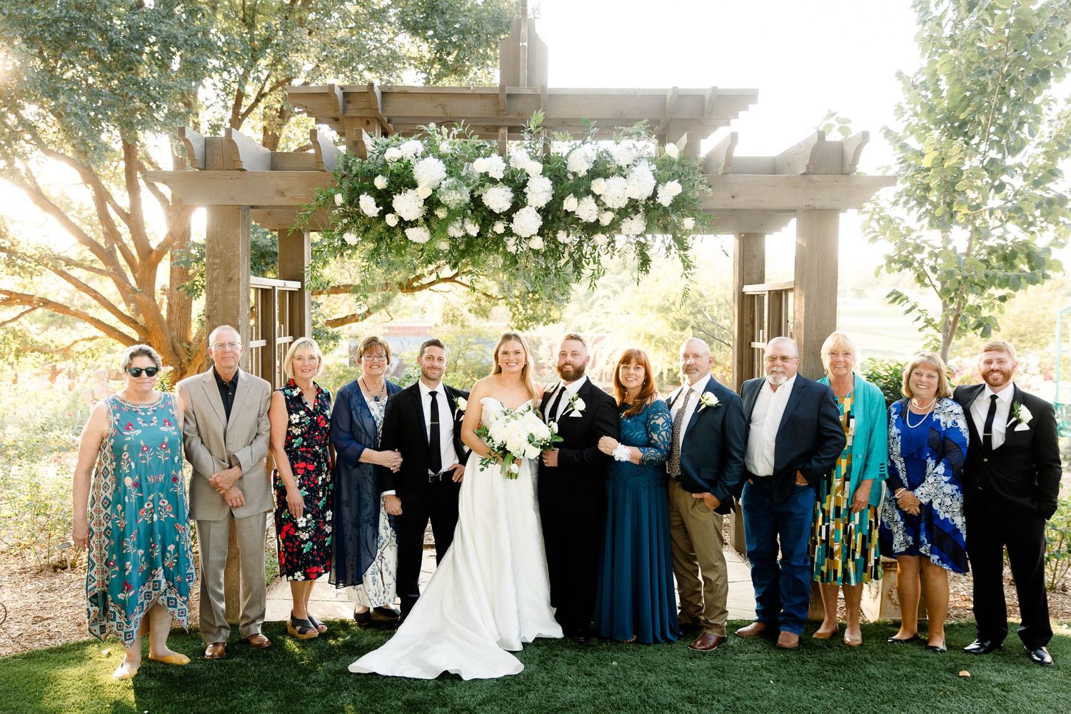 Large group wedding photo with bridal party and guests under decorated outdoor pavilion.