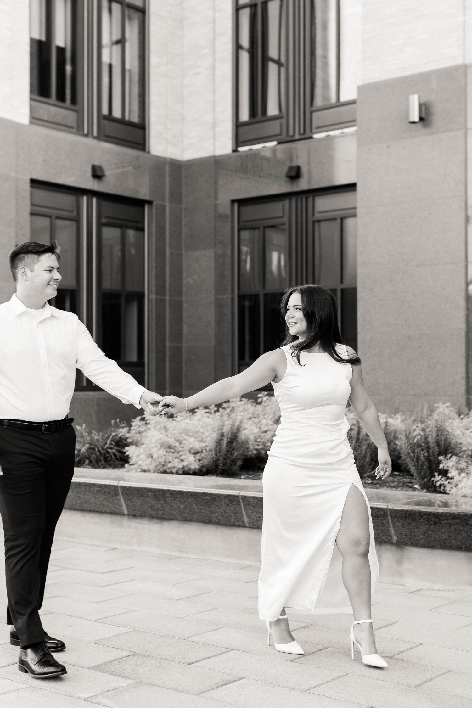 Black and white photo of couple dancing in formal wear outside modern building.