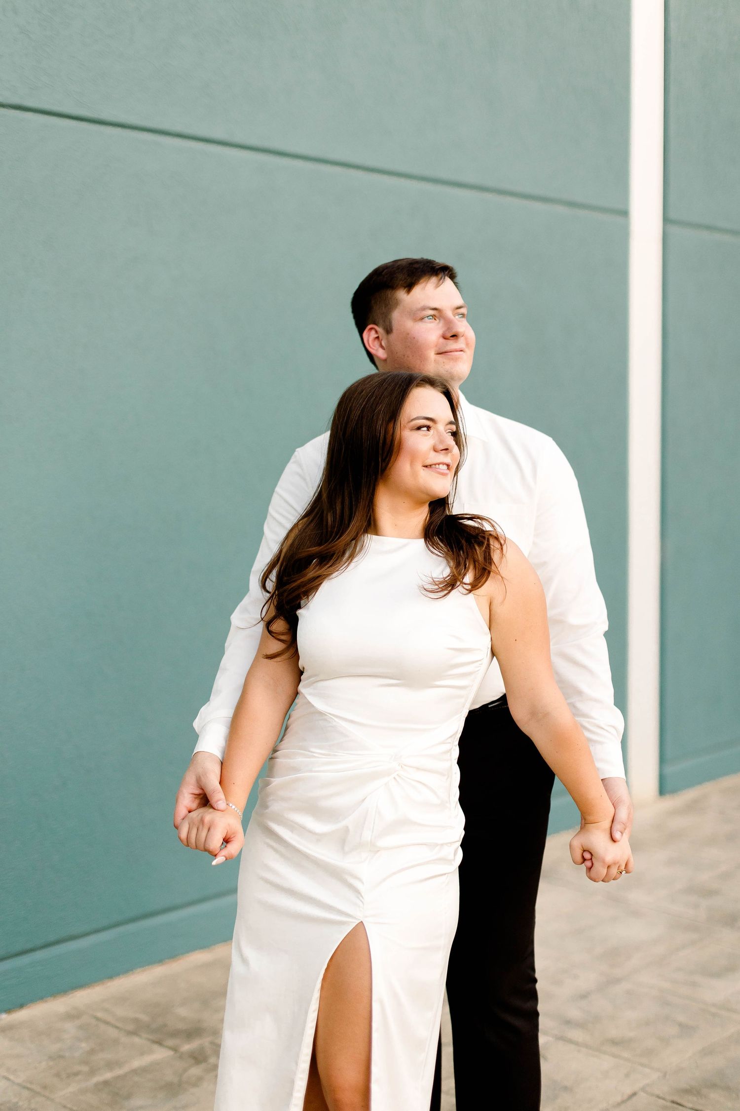 A joyful couple in white and black attire dances and laughs during their engagement photo session.
