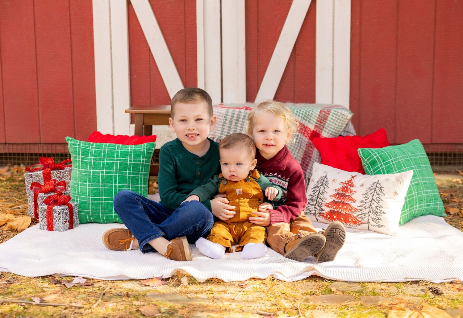 Holiday family photo setup with festive pillows and decorations against red barn.