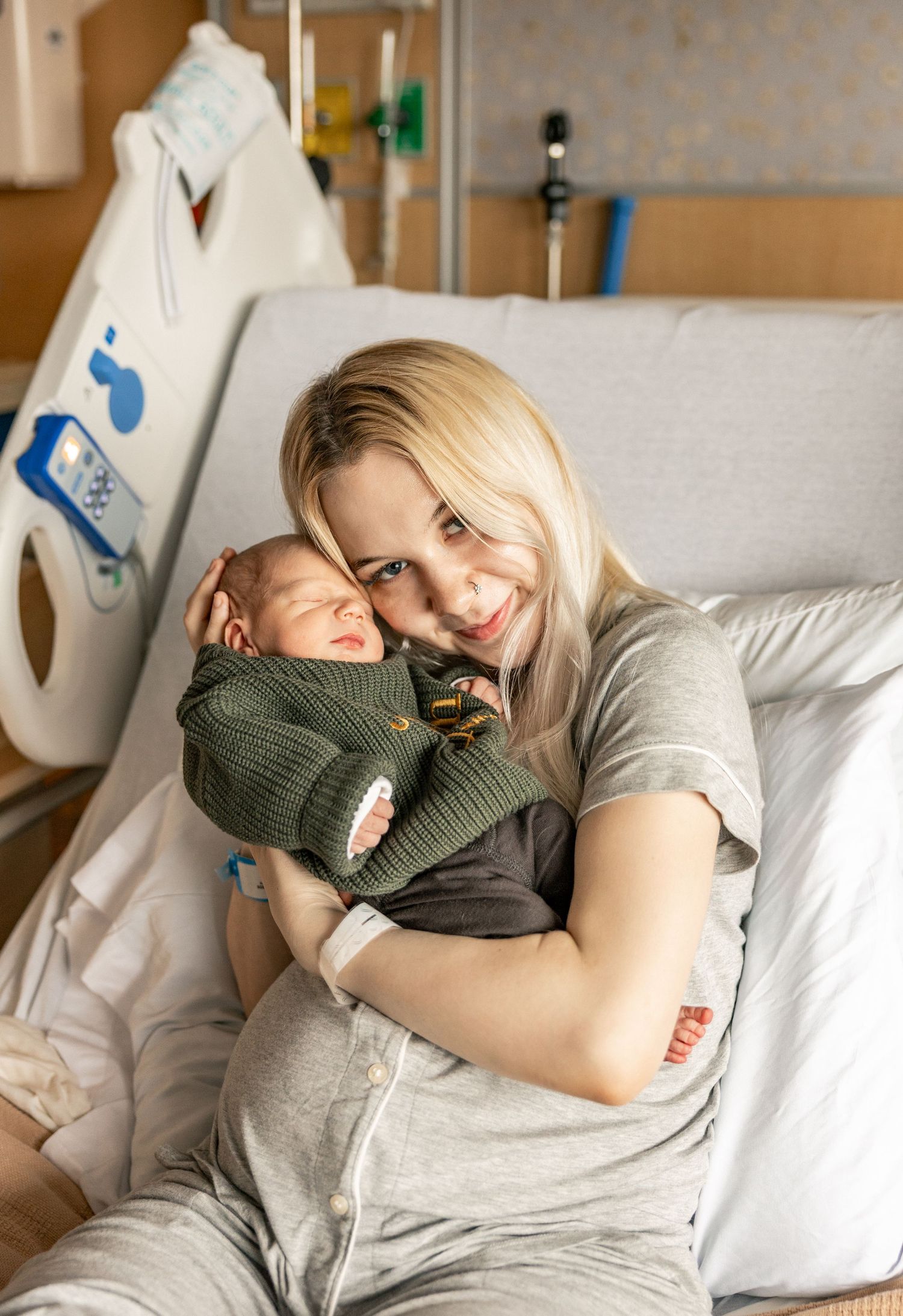 A tender moment captured in a hospital room as a parent embraces their newborn baby while resting on a medical bed.