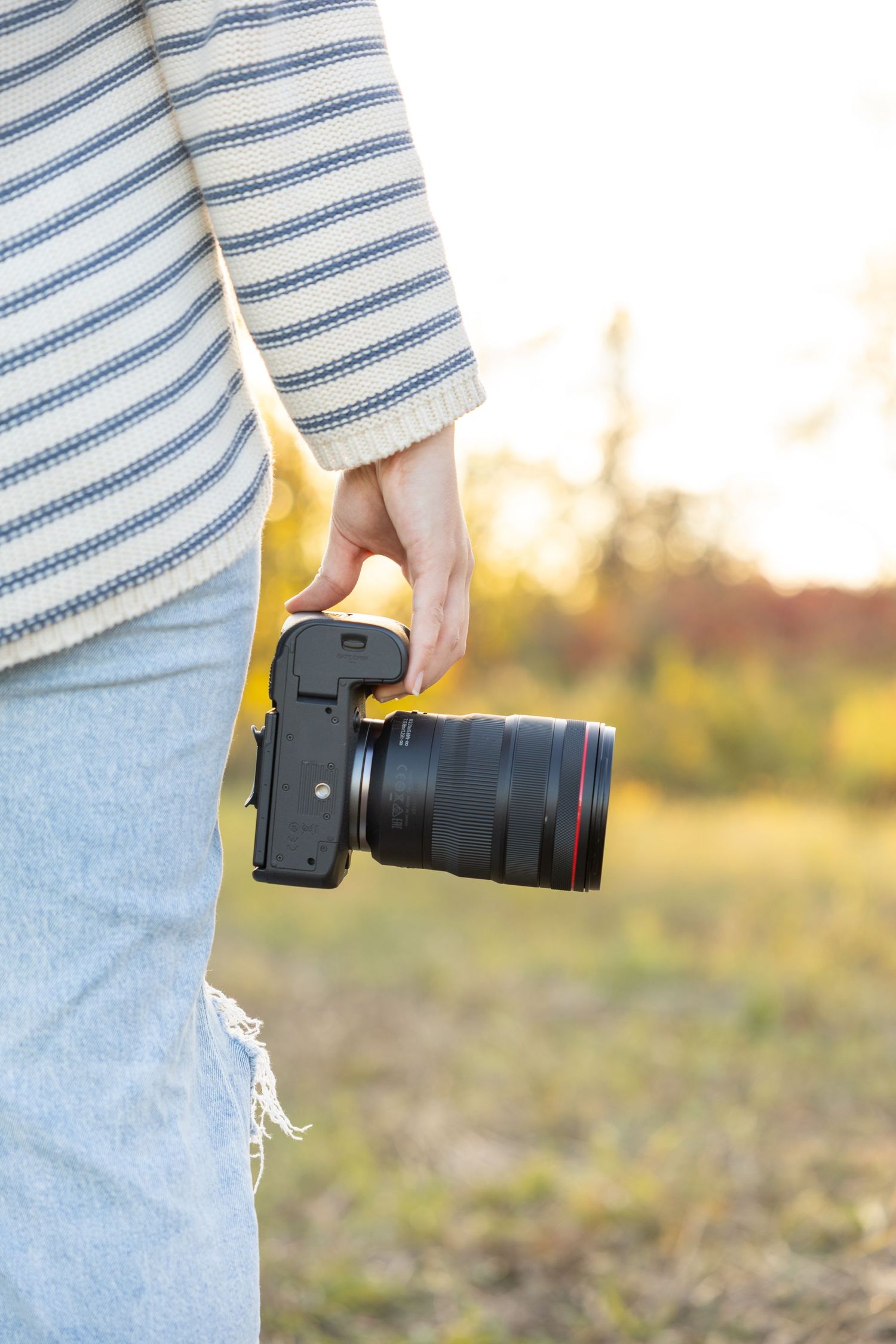 Close-up of hands holding professional camera with lens against sunset background.