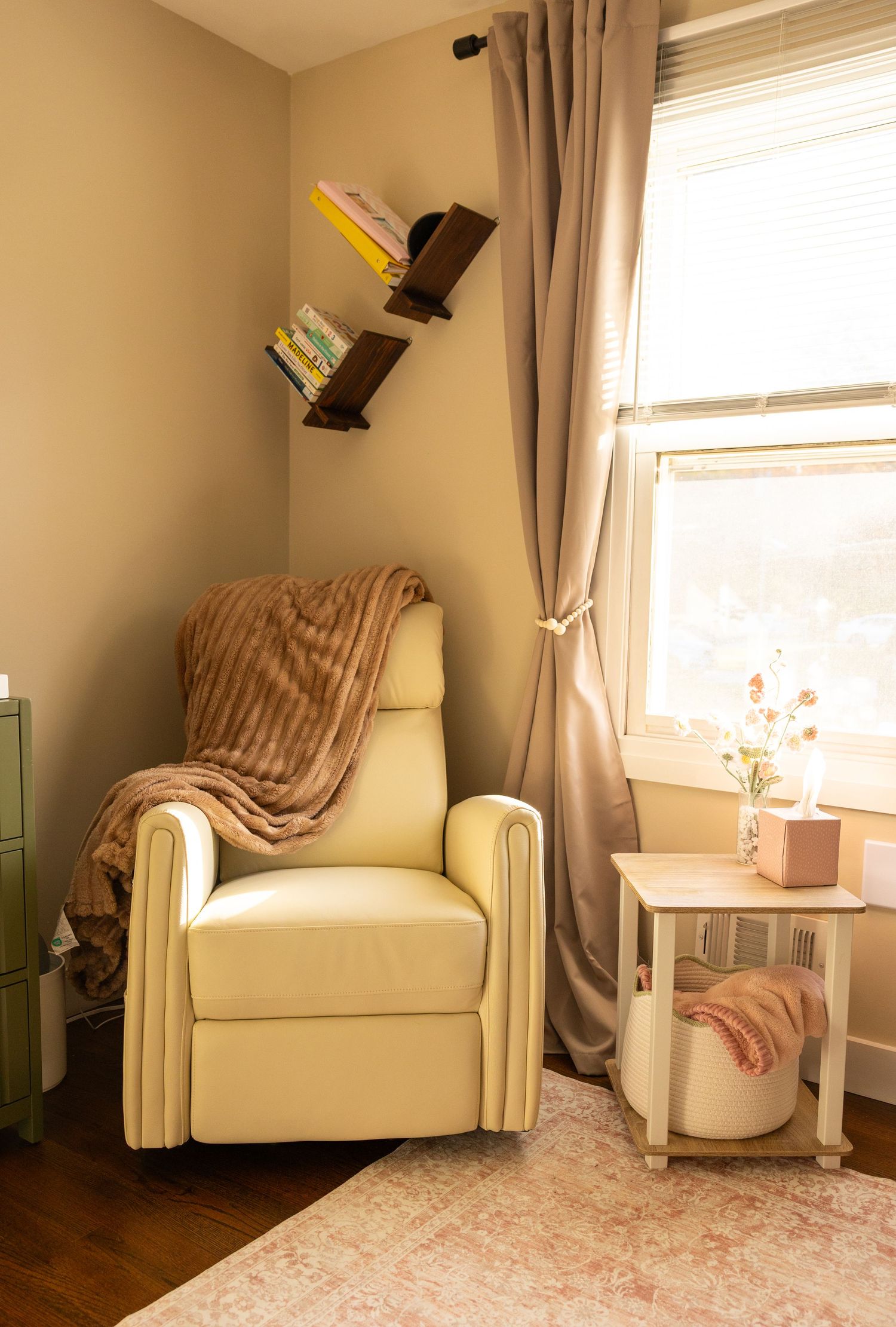 Cozy reading nook with cream armchair, floral rug, and natural light streaming through window with beige curtains.