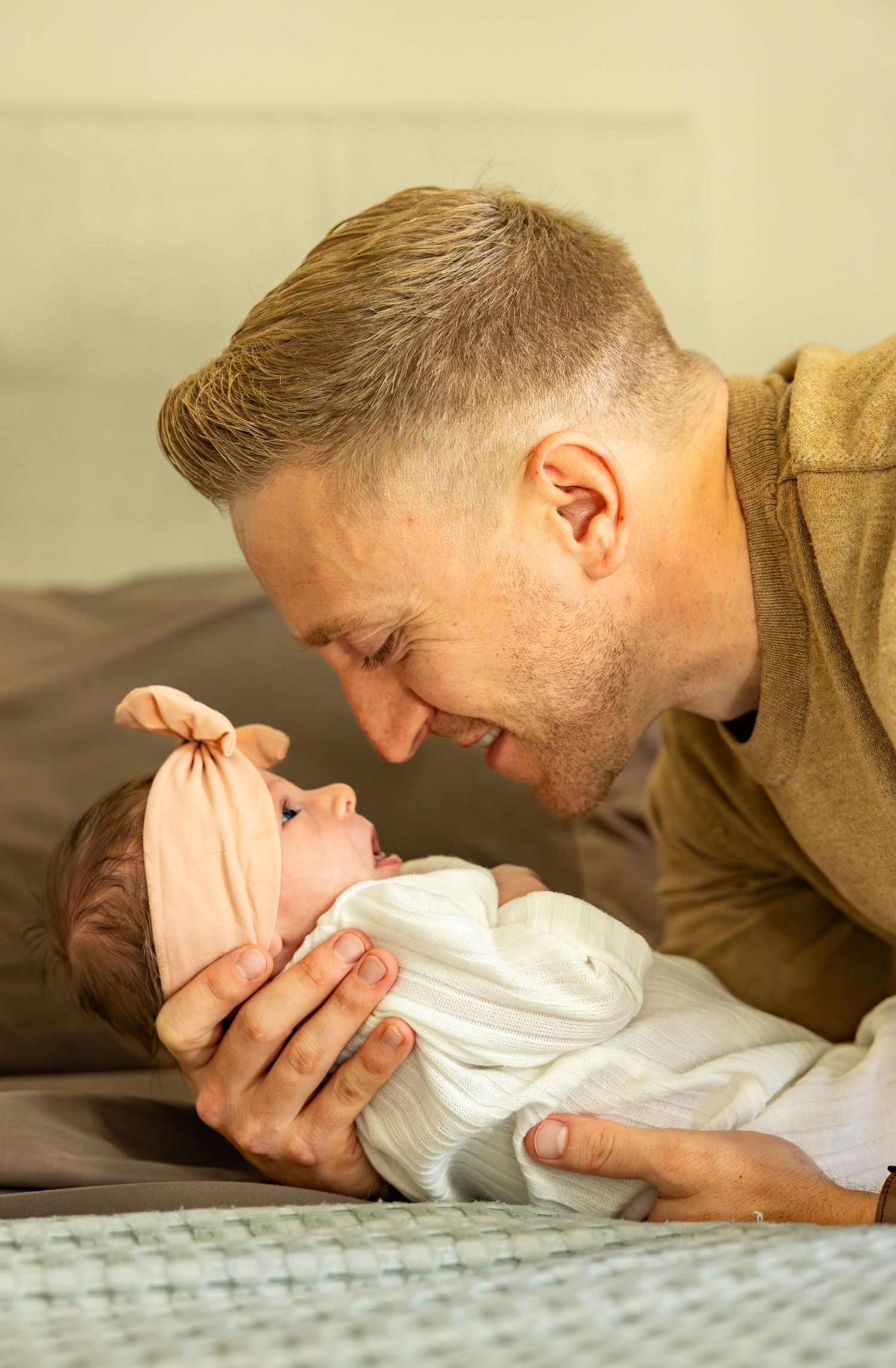 A person in a tan sweater tenderly holding a newborn wrapped in white.