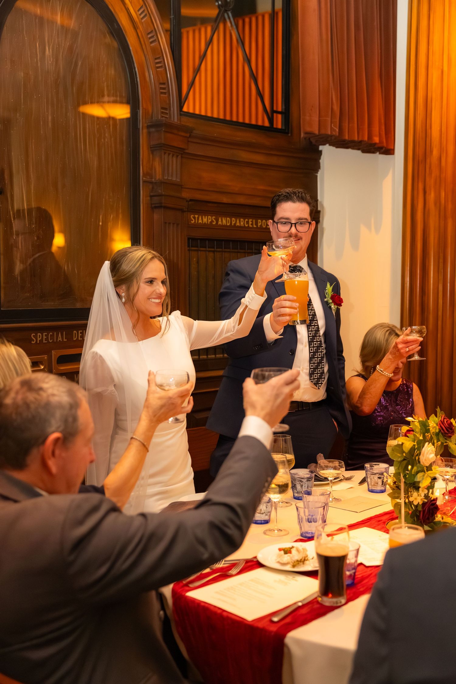 Wedding reception guests raising glasses in a toast at an elegant wood-paneled venue.