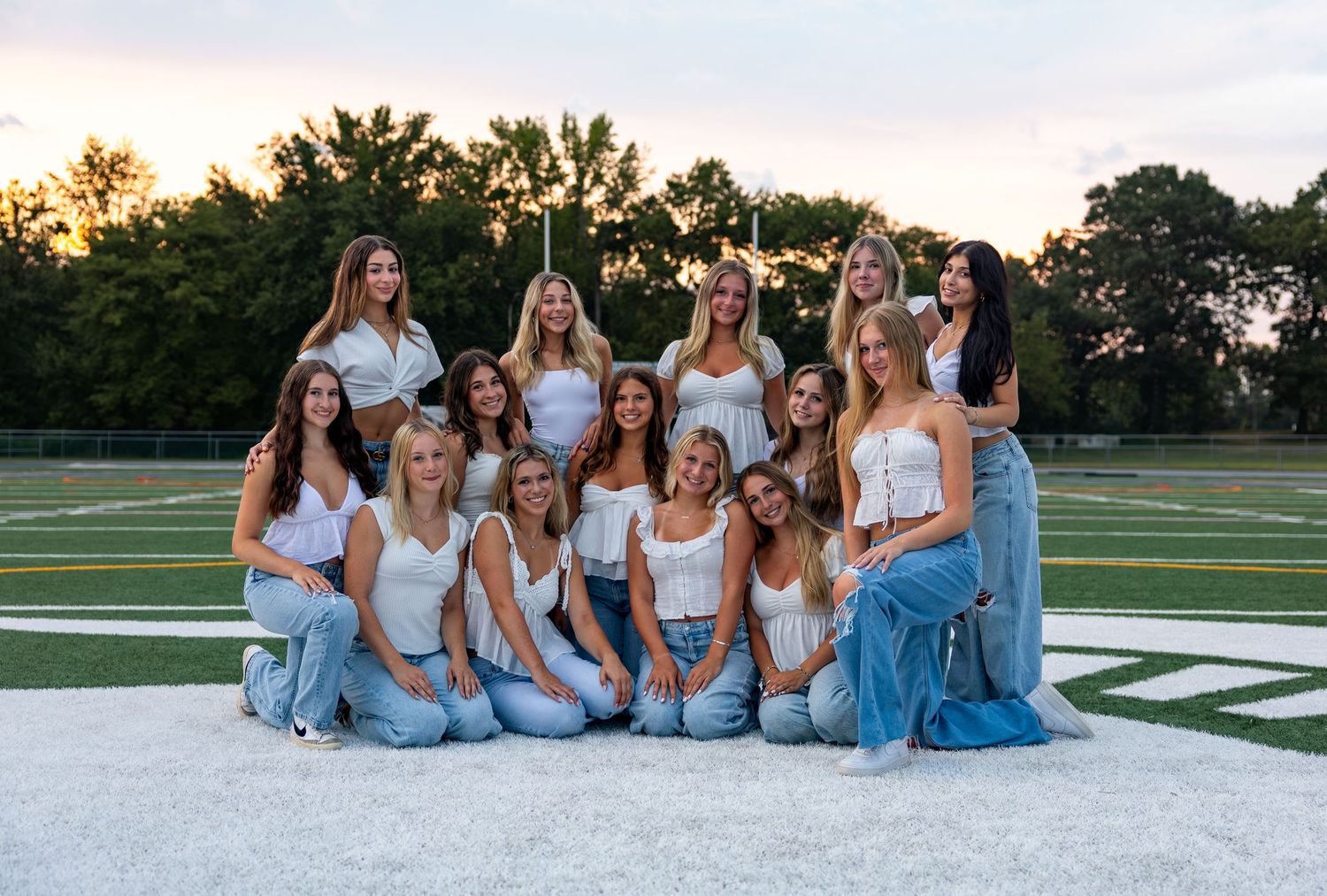 Group photo of cheerleaders in matching light blue outfits sitting together at sunset.