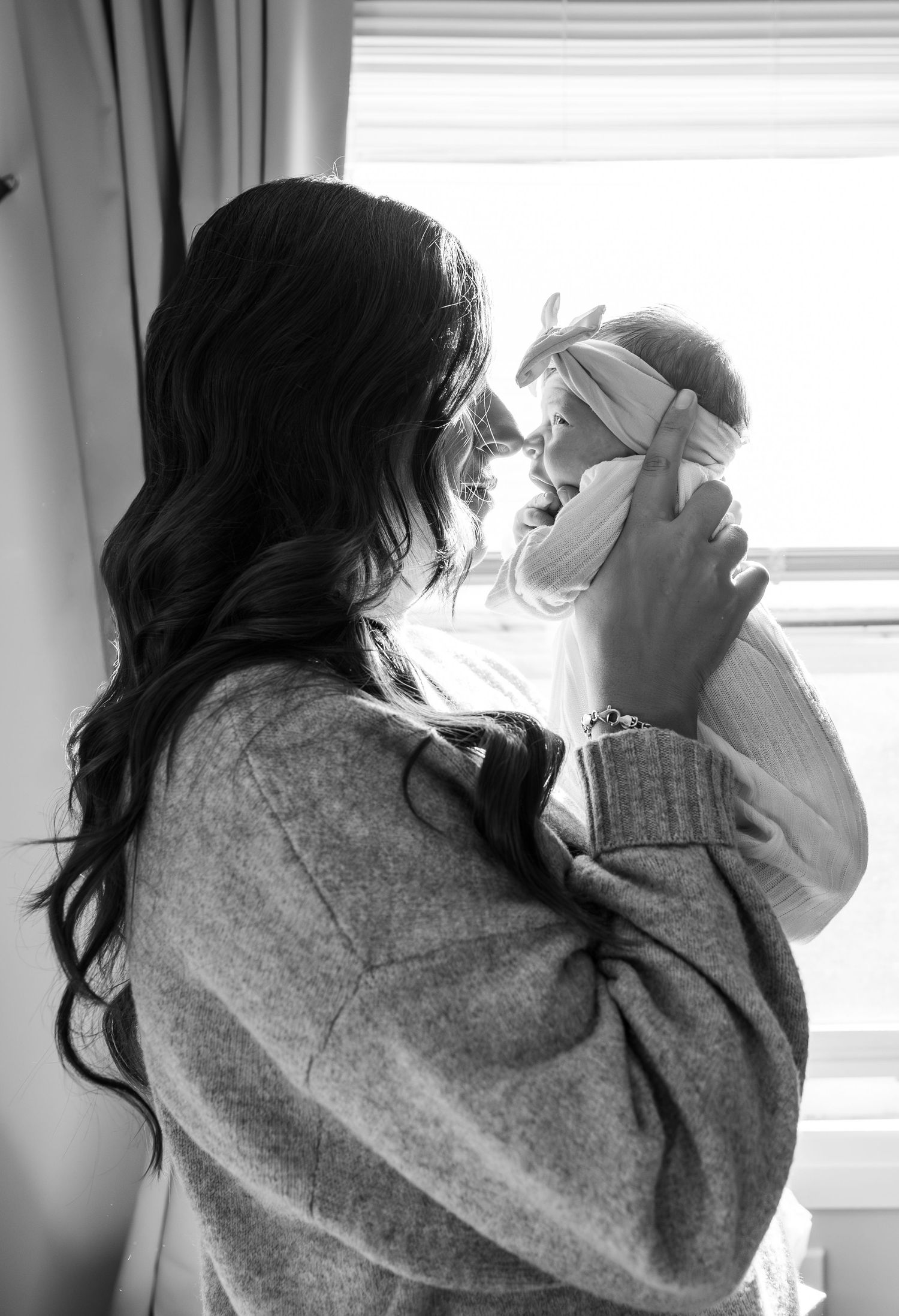A tender black and white moment between parent and baby by a window in soft natural light.