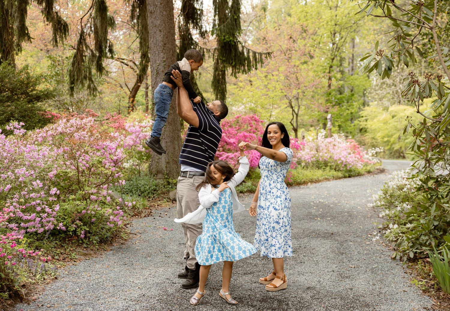 Family of four playing in a garden path surrounded by blooming pink azaleas and Spanish moss-draped trees.