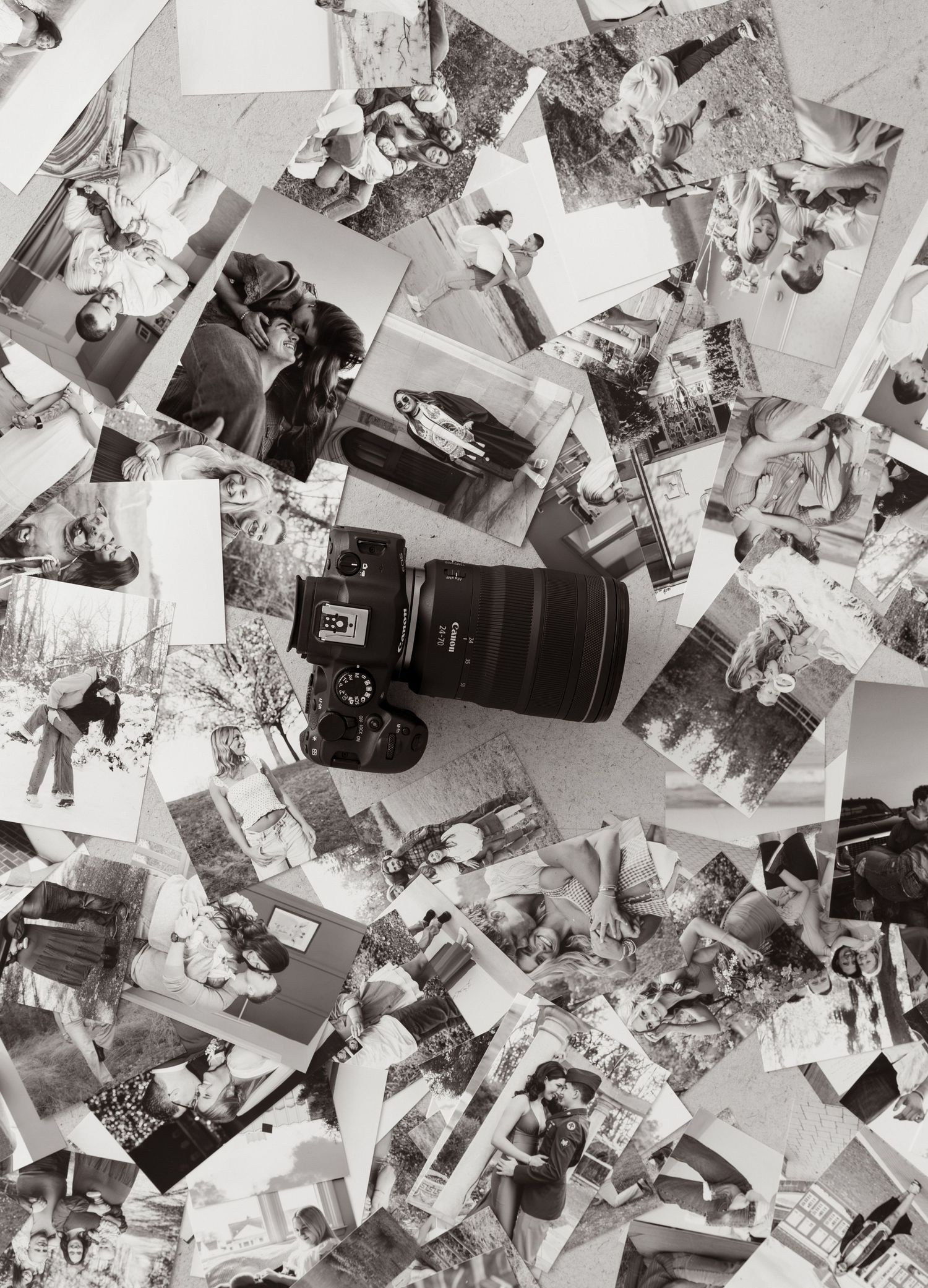 Black and white photo of a DSLR camera resting on a scattered pile of printed photographs on a flat surface.