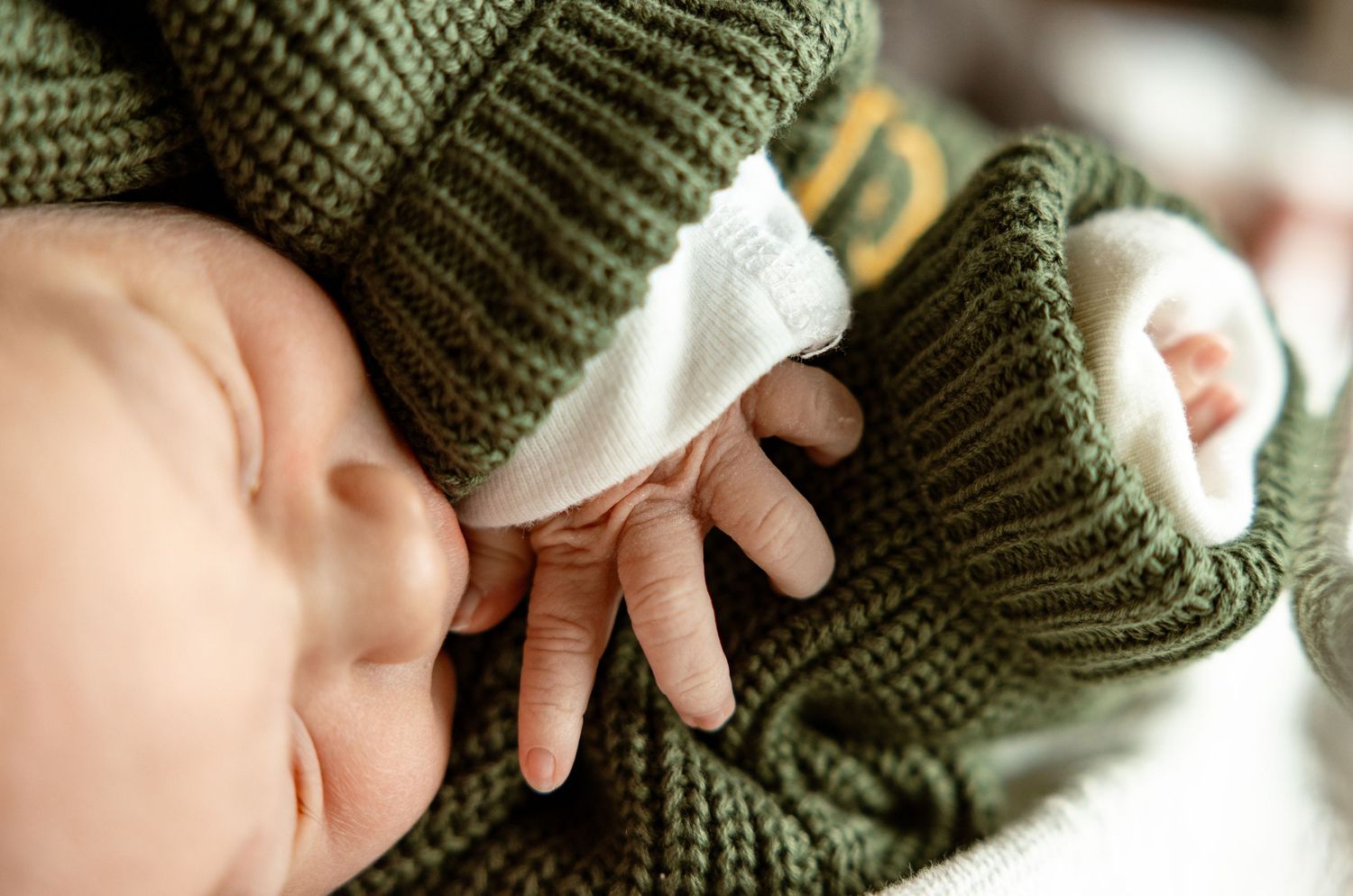 Close-up of hands knitting with olive green yarn and white knitting needles creating a ribbed pattern.