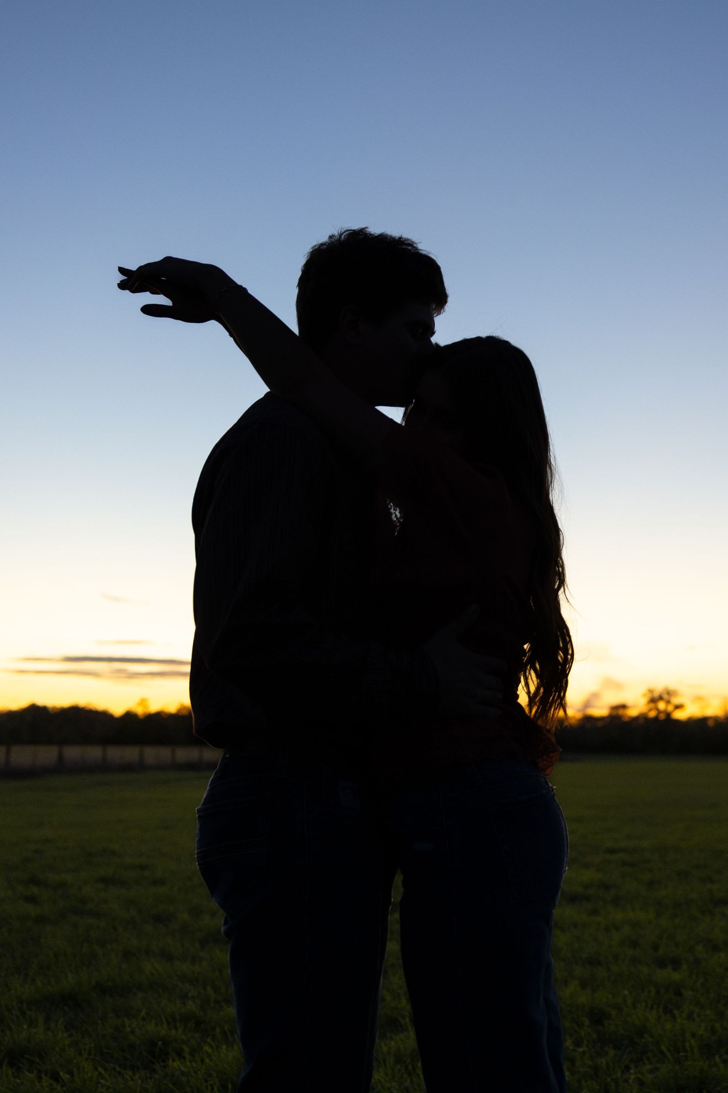Silhouettes of two people standing together in a field at dusk.