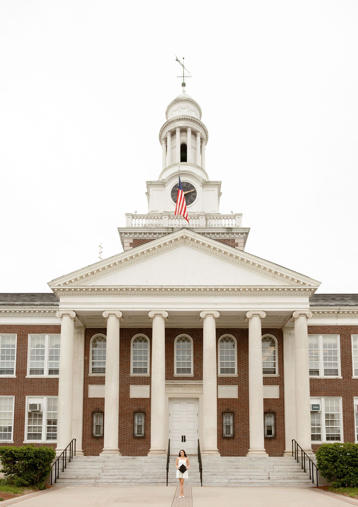 Woman standing on steps of a classic brick colonial building with white columns and American flag cupola.