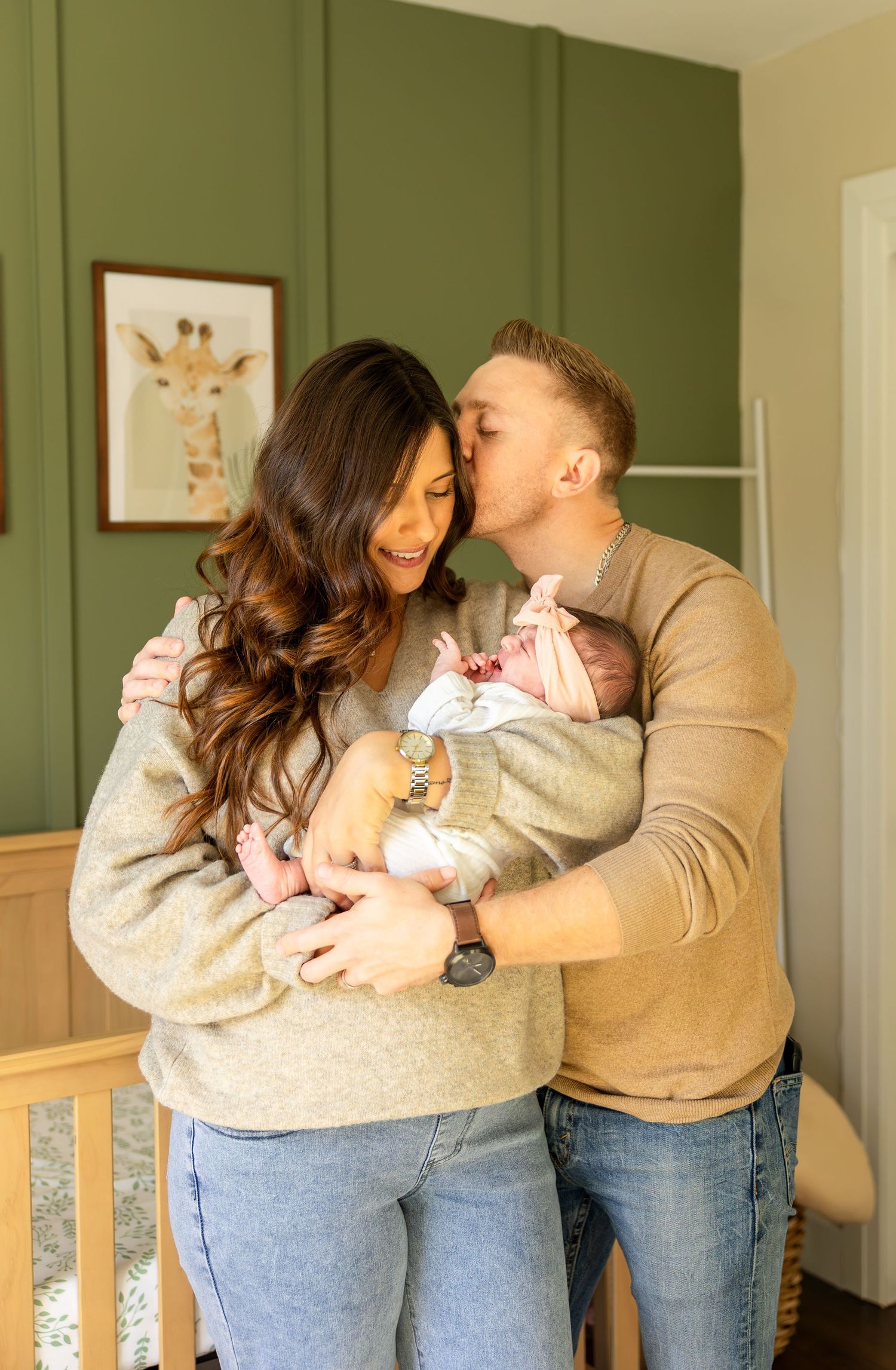Parents sharing loving moments with their newborn in a room with sage green walls.