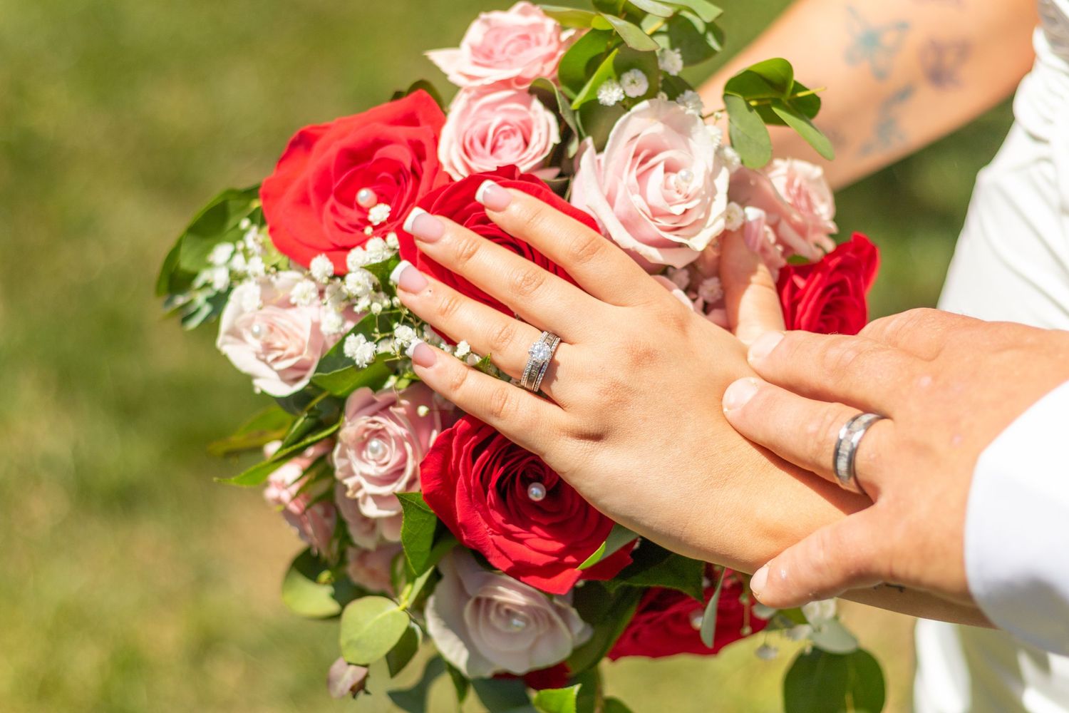 Close-up of hands holding a bouquet of red and pink roses.