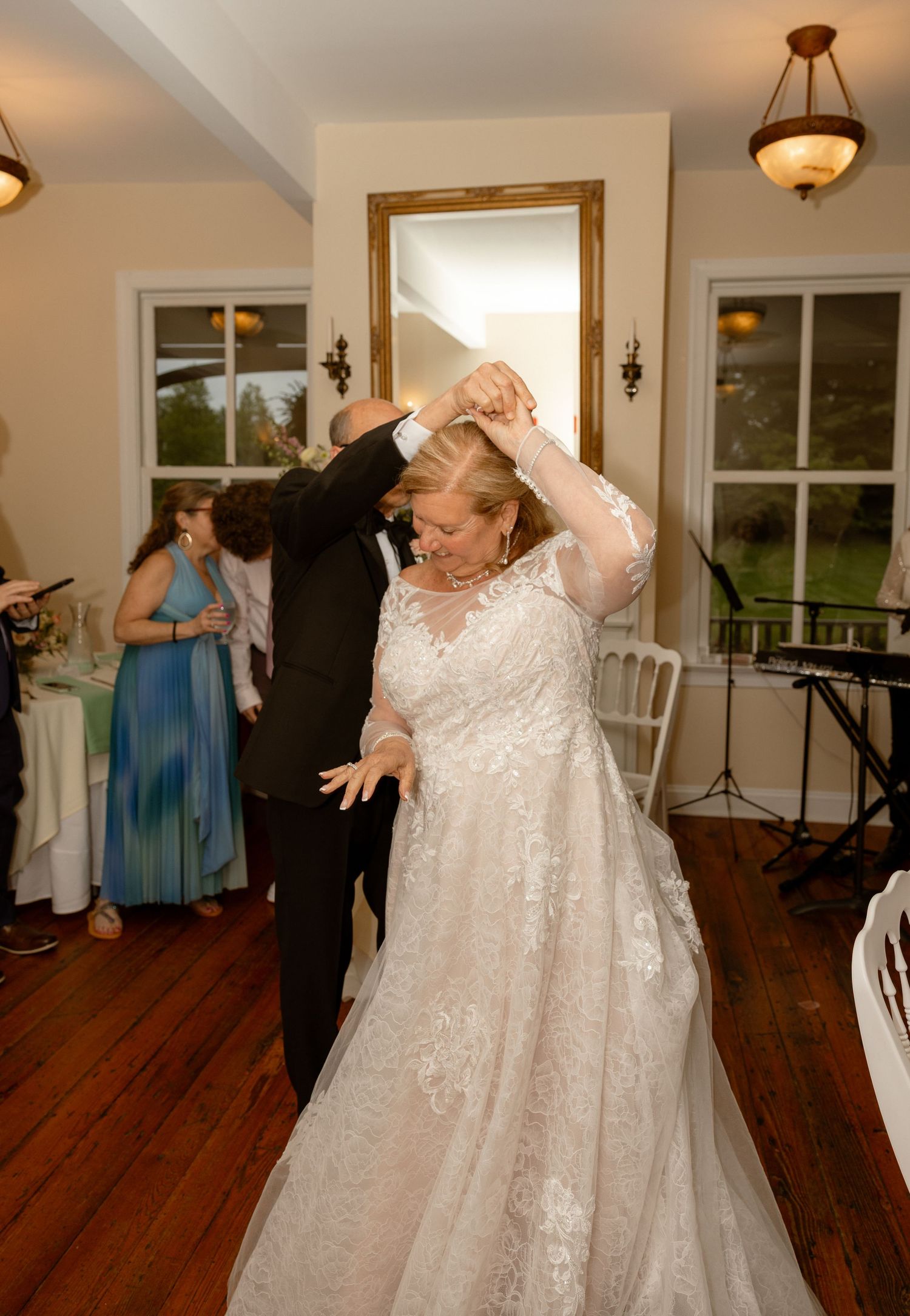 Bride in lace gown twirls with groom in tuxedo during wedding reception first dance in elegant venue.