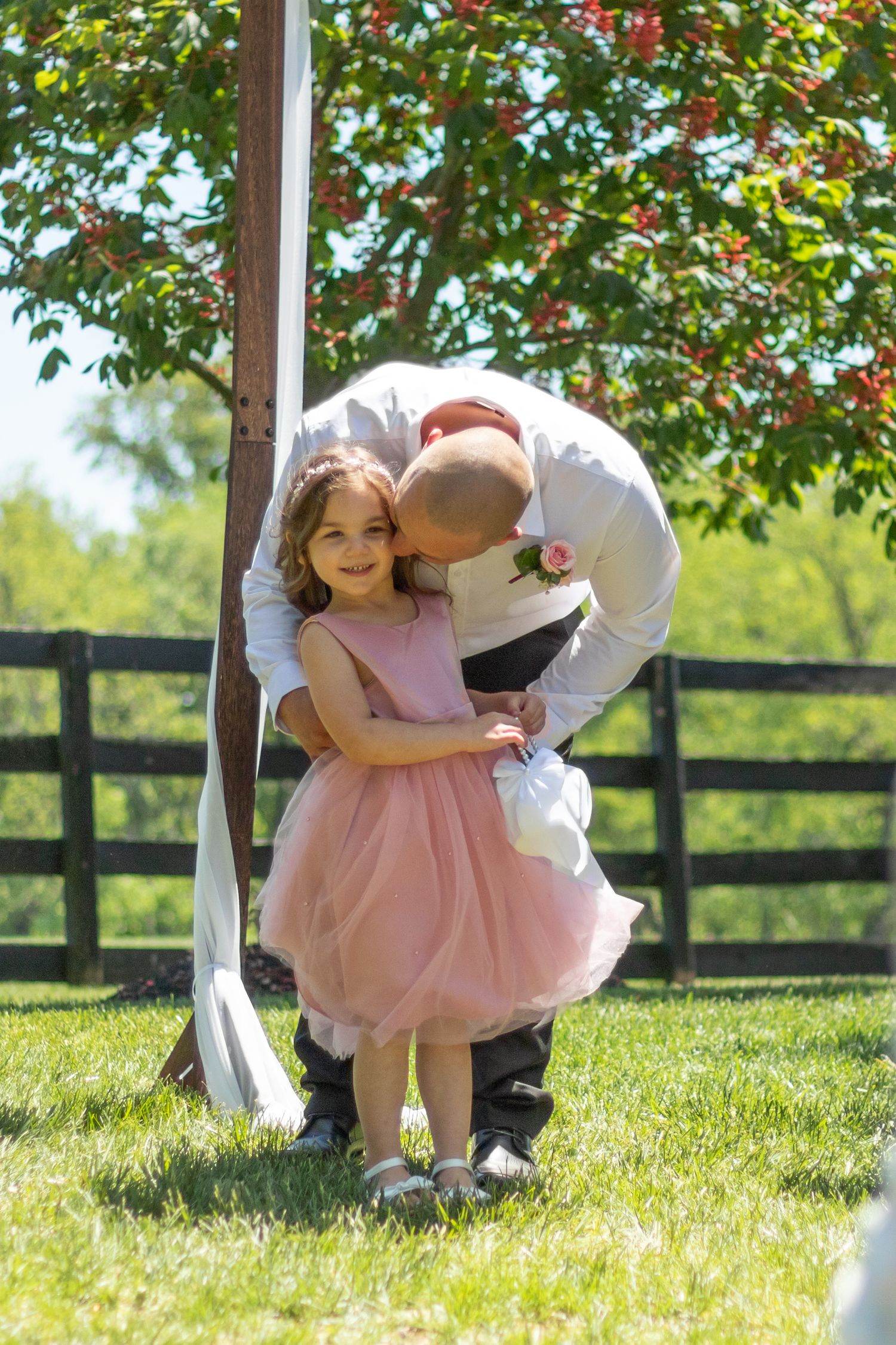 A tender moment captured under a floral-decorated arbor on a sunny lawn.