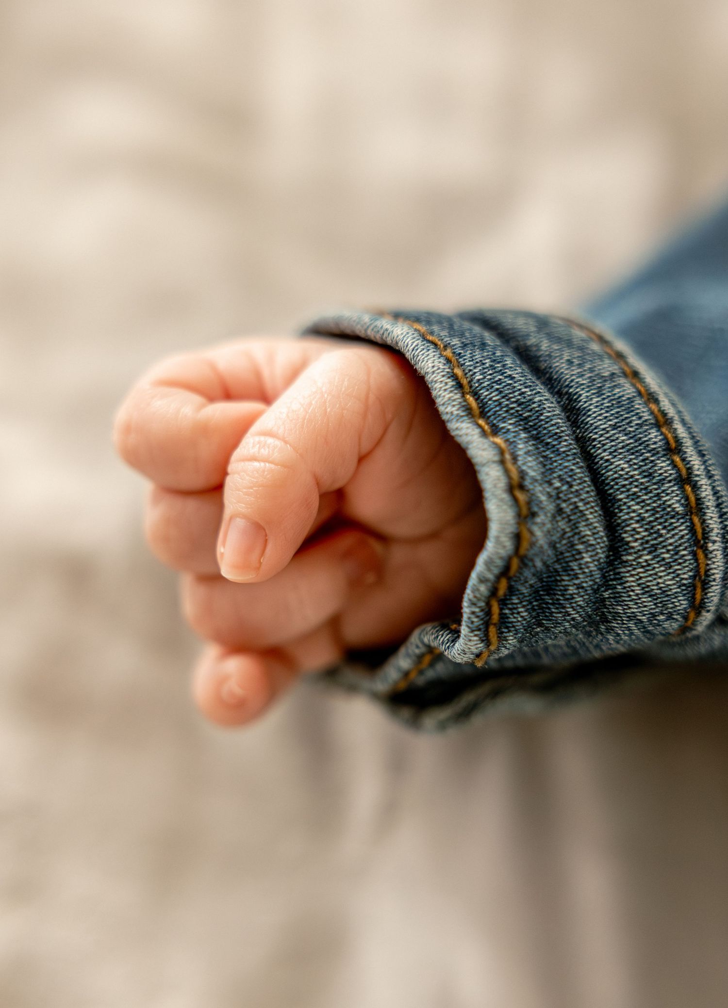 Close-up of a baby's tiny hand wearing an oversized blue denim jacket sleeve, fingers gently curled.