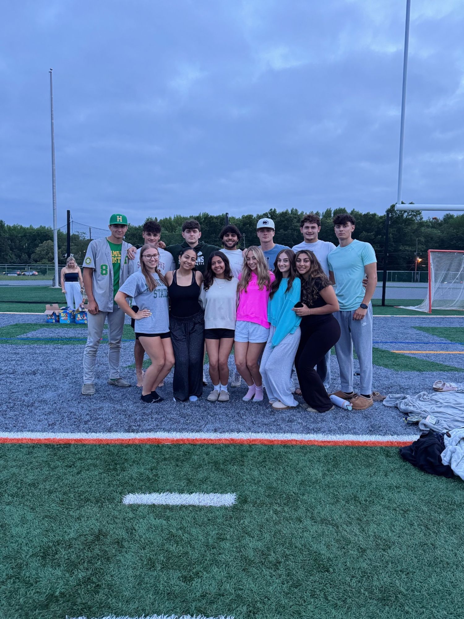 Group photo series taken outdoors at dusk near a sports field or recreational area.