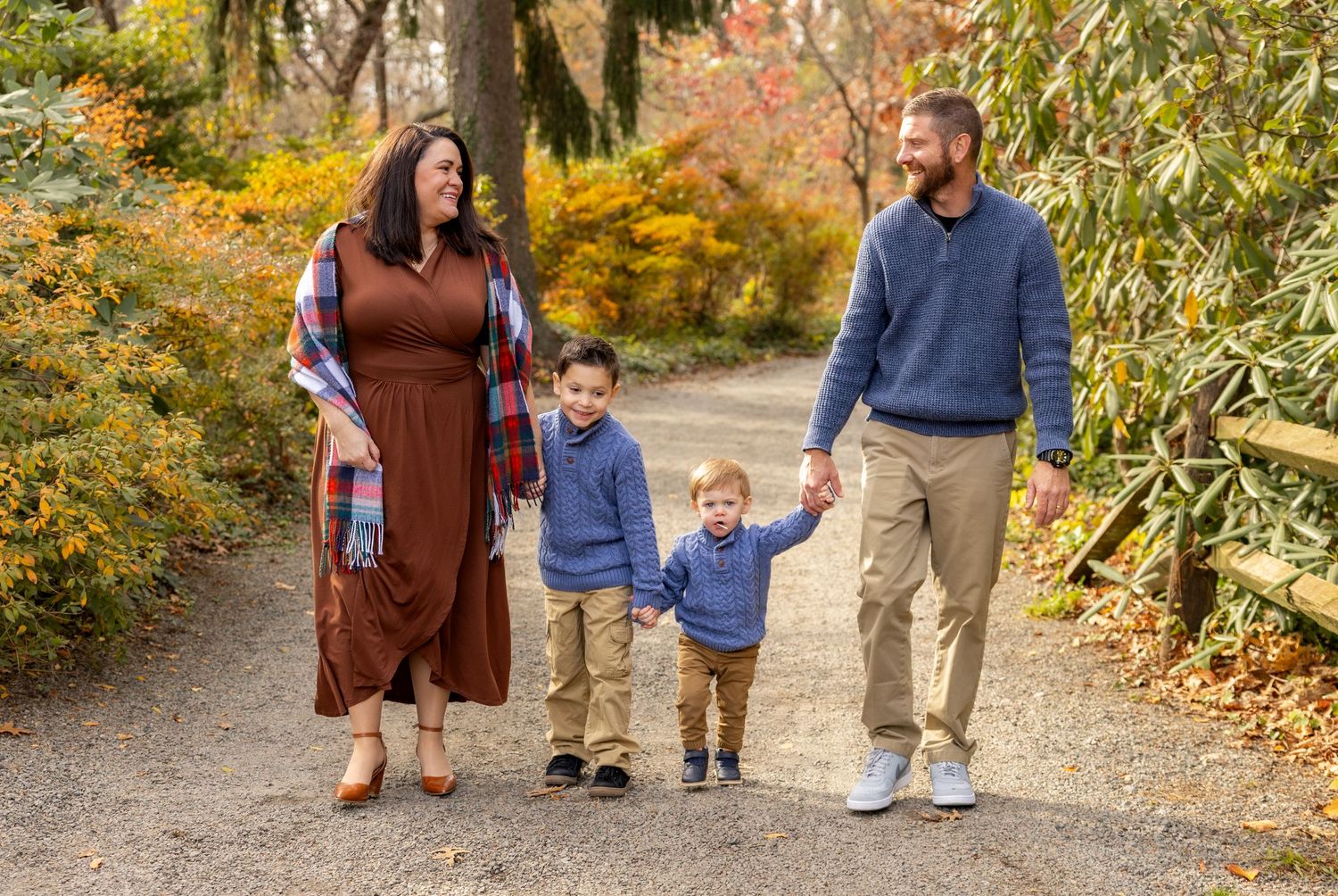 A family walking together on an autumn path lined with colorful fall foliage.