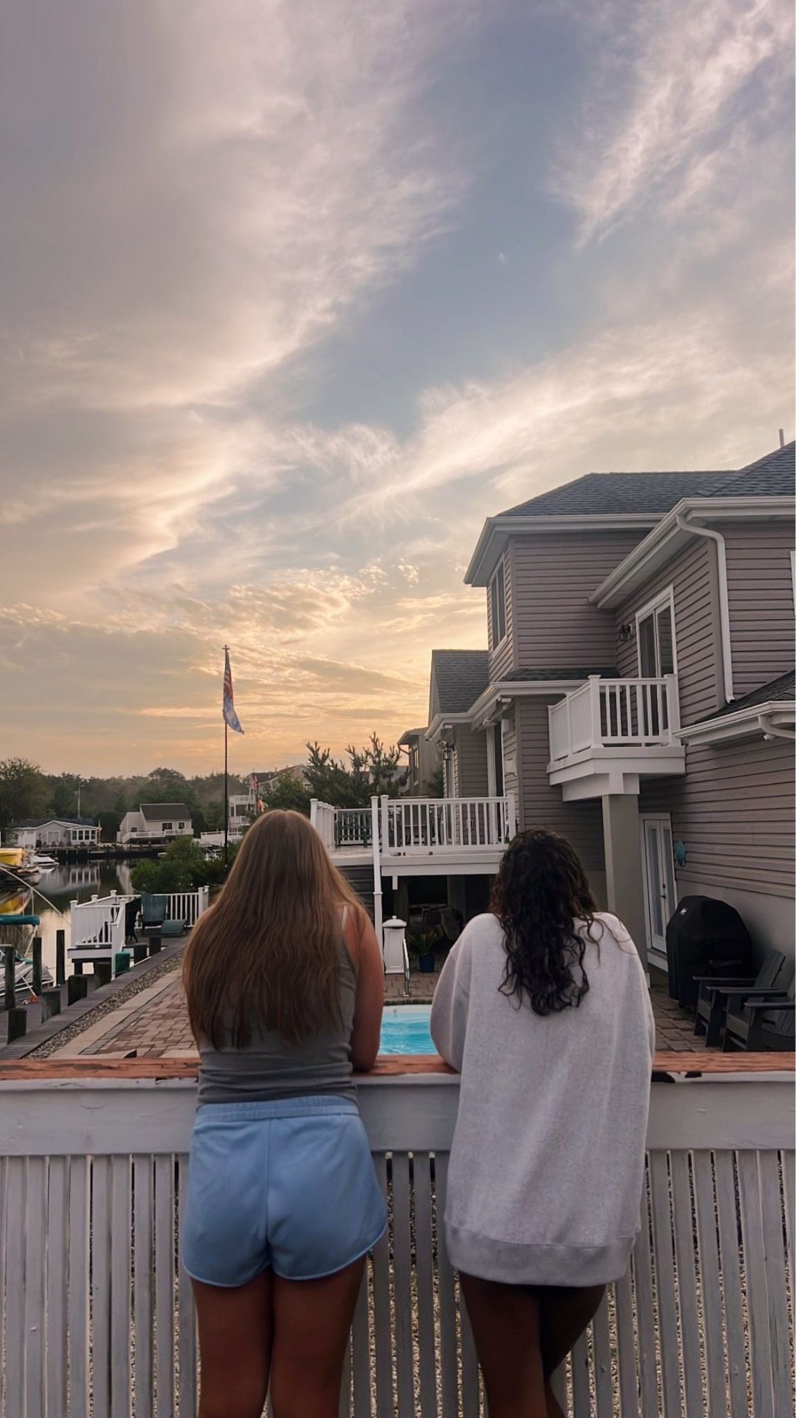 People watching sunset from a deck overlooking residential homes with dramatic sky in background.