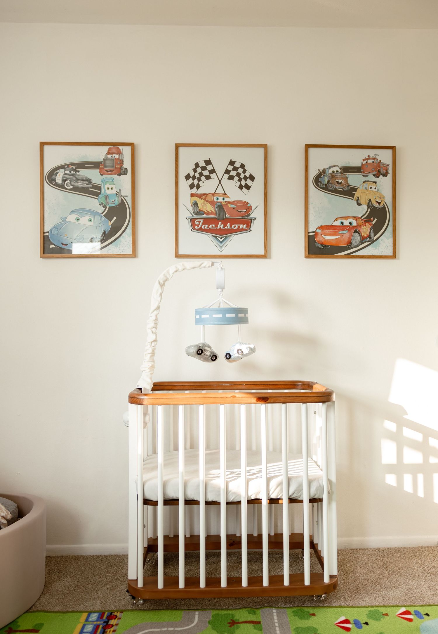 A nursery with three framed Cars movie prints above a white crib, featuring racing themes and checkered flags on the wall.